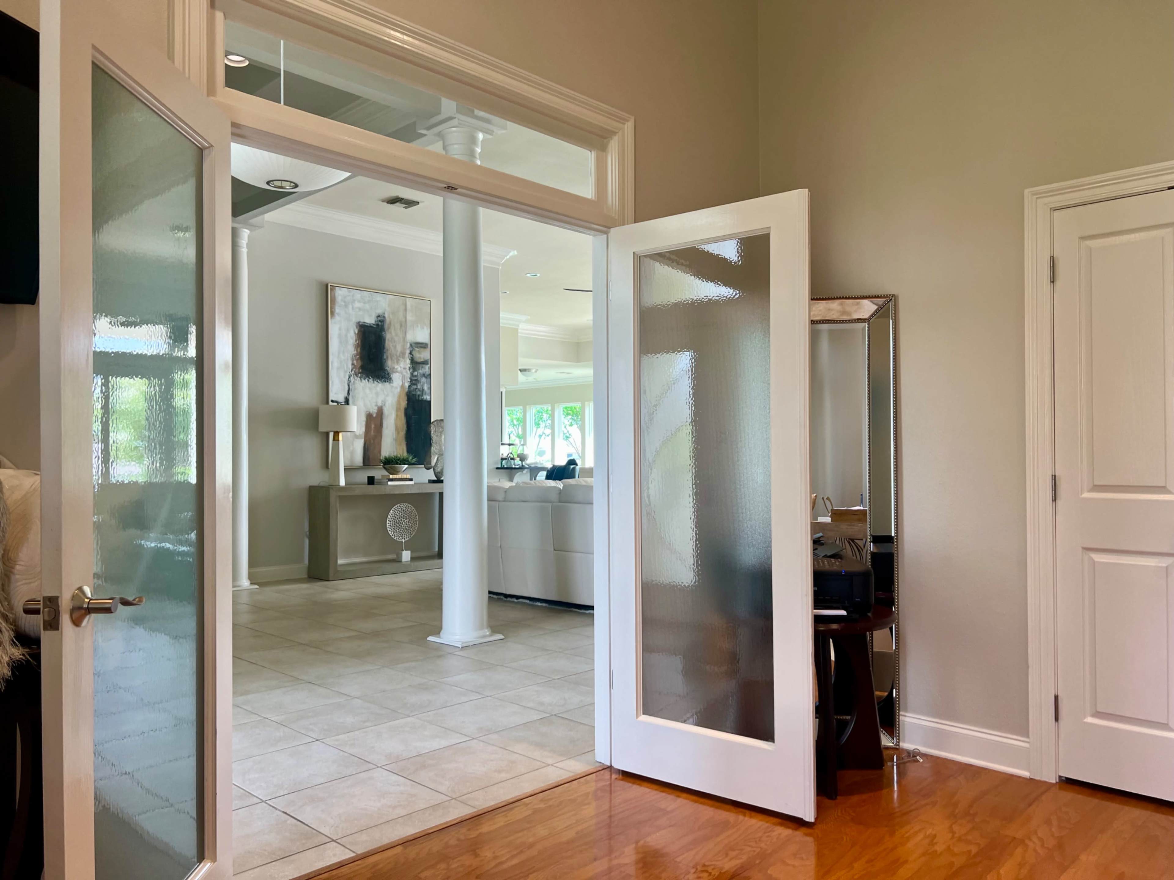An open doorway leading into a spacious interior with tiled floors, glass doors, and a glimpse of modern furnishings.