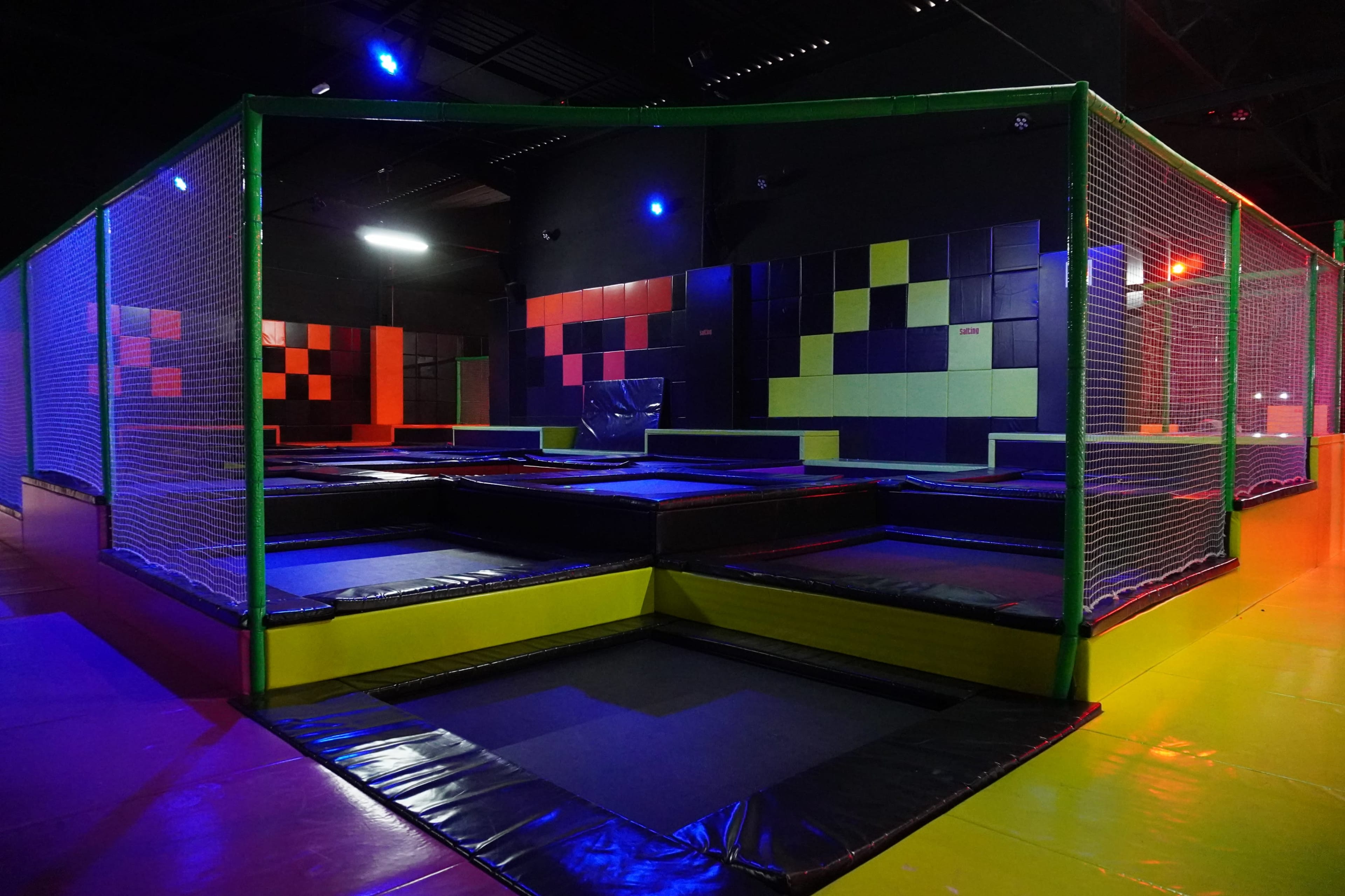 An indoor trampoline park with multiple trampoline areas enclosed by safety nets and colorful wall panels.