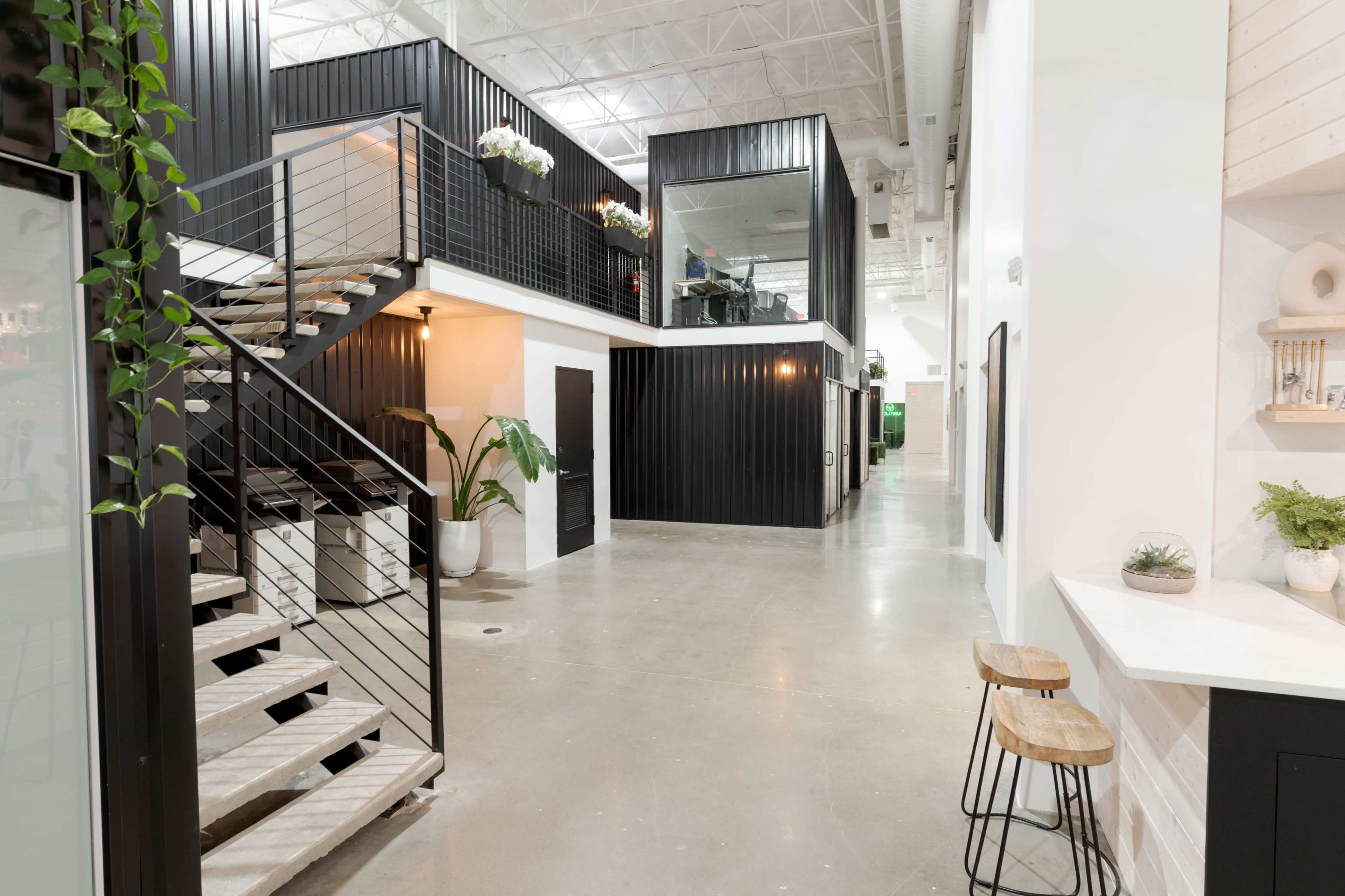 A modern interior space featuring a staircase with a metal railing, open areas, and office facilities behind glass partitions.