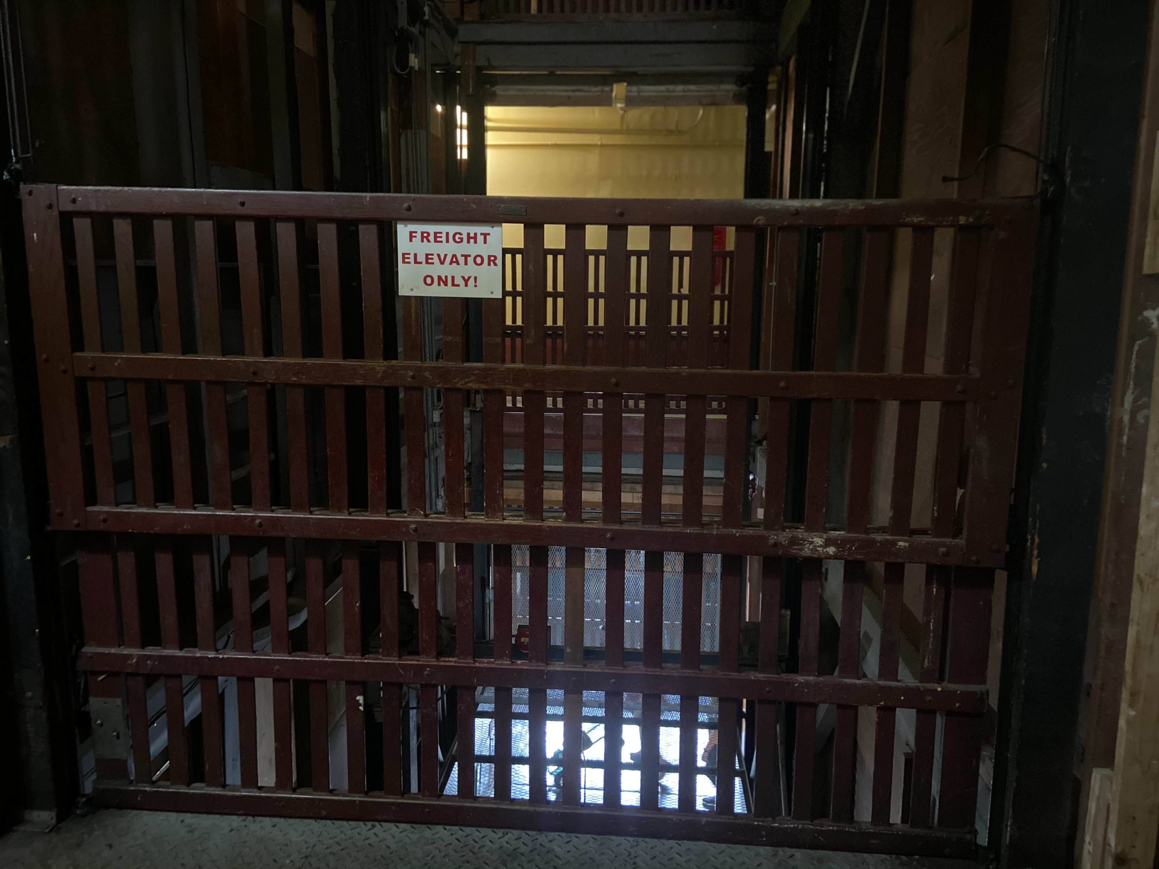 A barred gate with a sign that reads "FREIGHT ELEVATOR ONLY!" in a dimly lit stairwell.