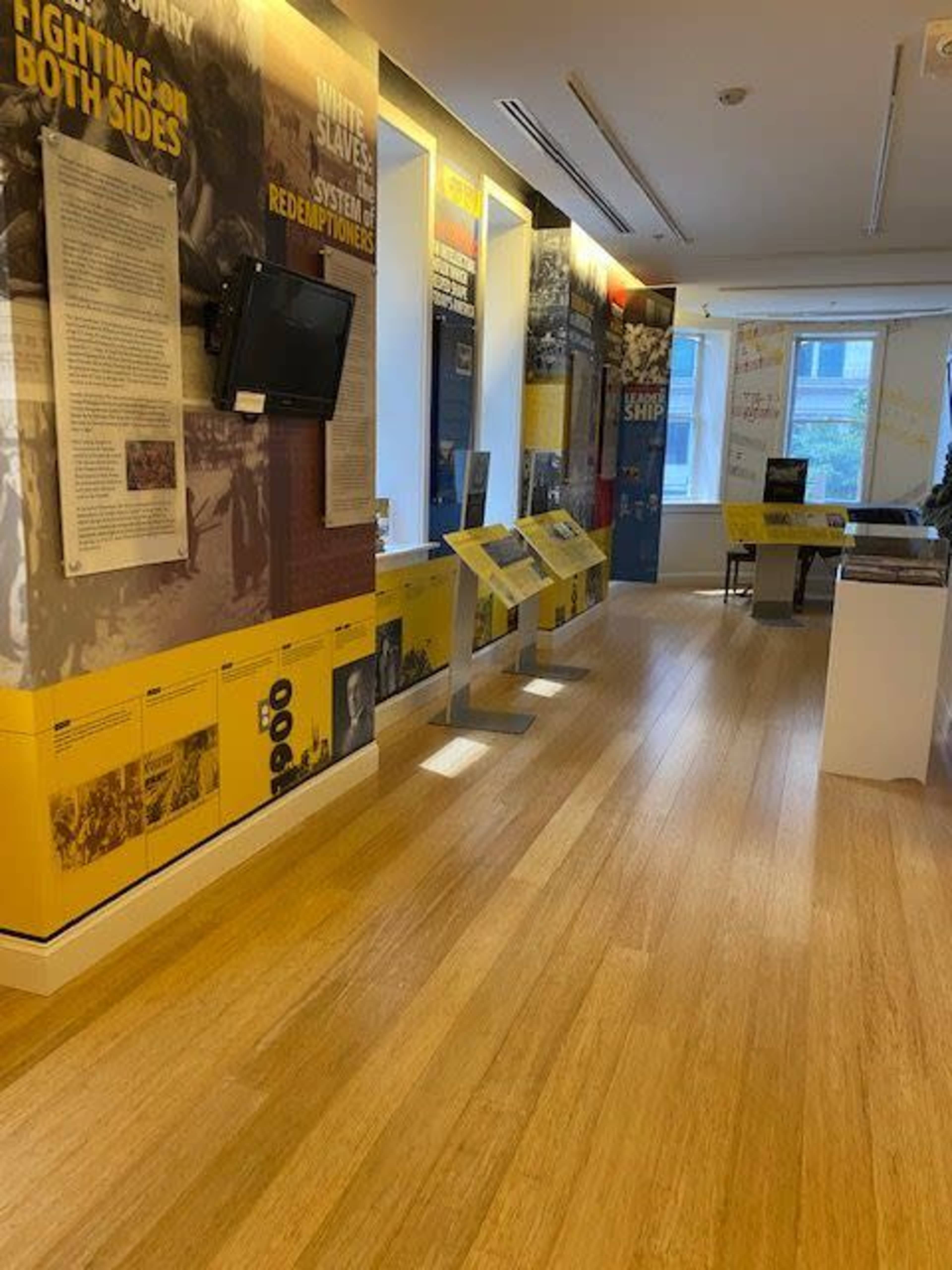 An interior view of a museum exhibit with informative panels and displays arranged along wooden floors.