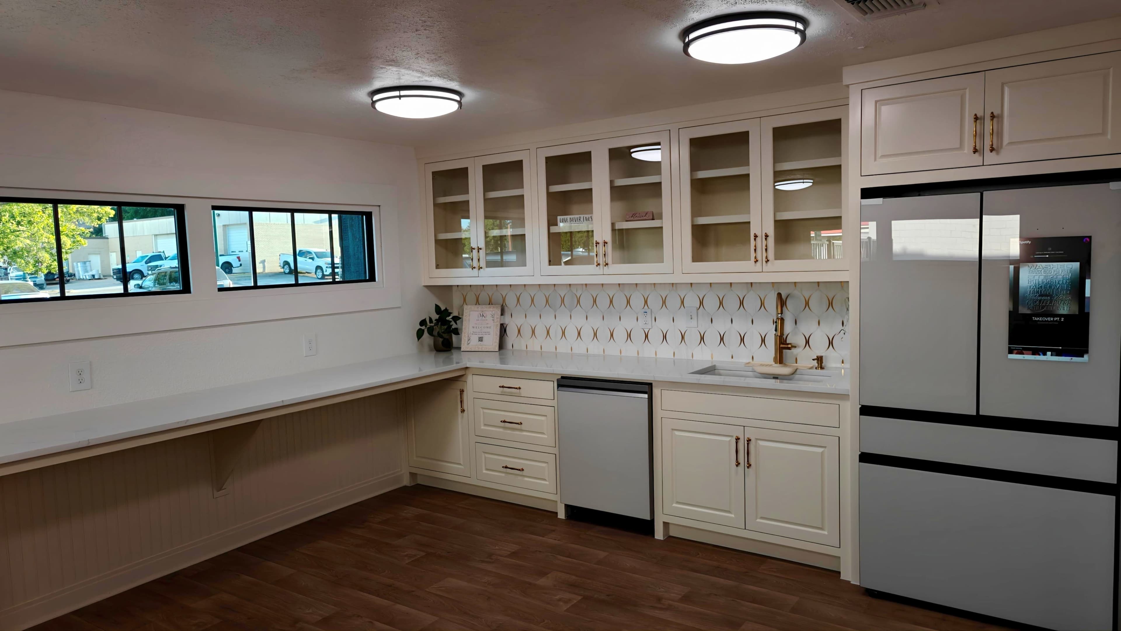 The image shows a modern kitchen with white cabinetry, a built-in countertop, and stainless steel appliances, including a refrigerator and dishwasher.