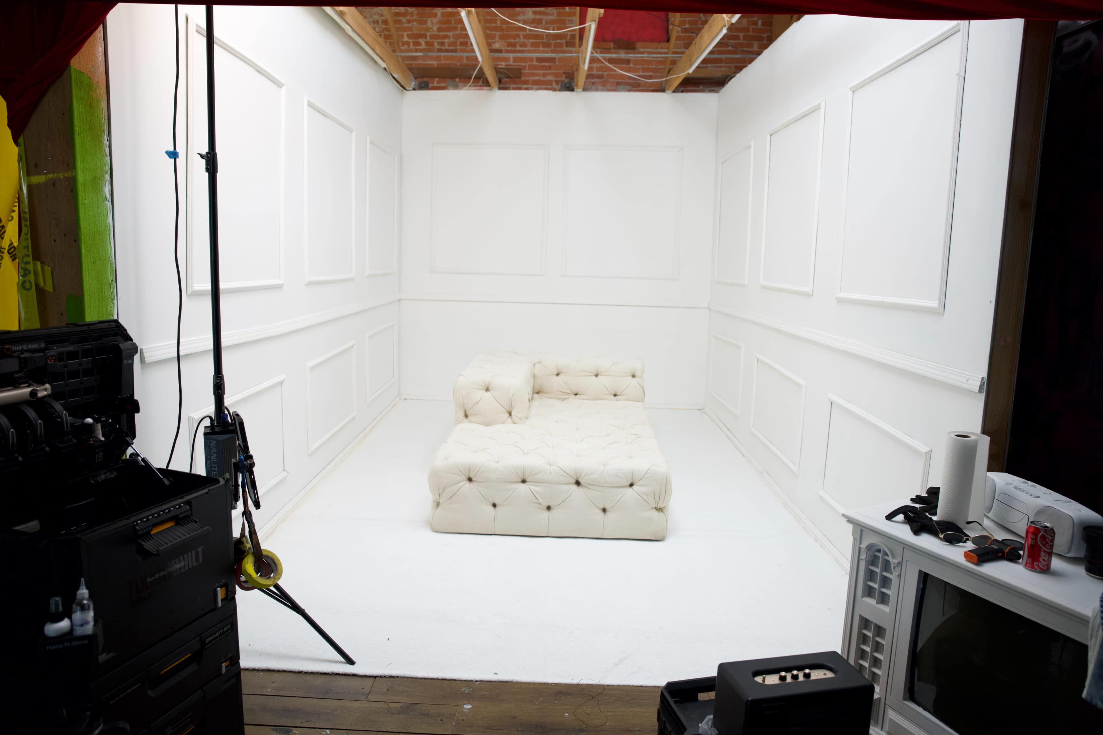 The image shows a minimalist white room with a tufted cream-colored sofa in the center, surrounded by plain white walls.