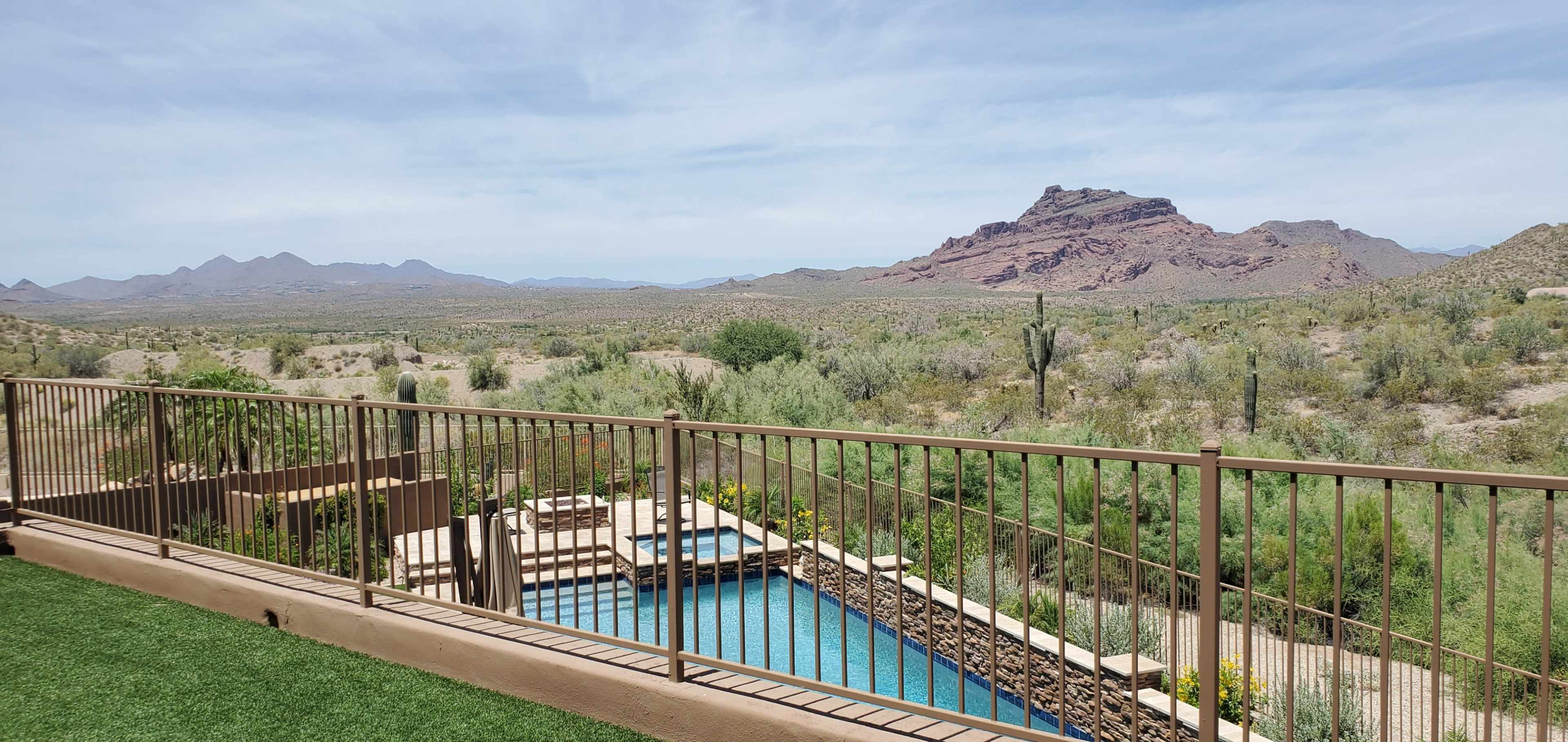 The image shows a swimming pool surrounded by a fenced patio, overlooking a mountainous desert landscape.