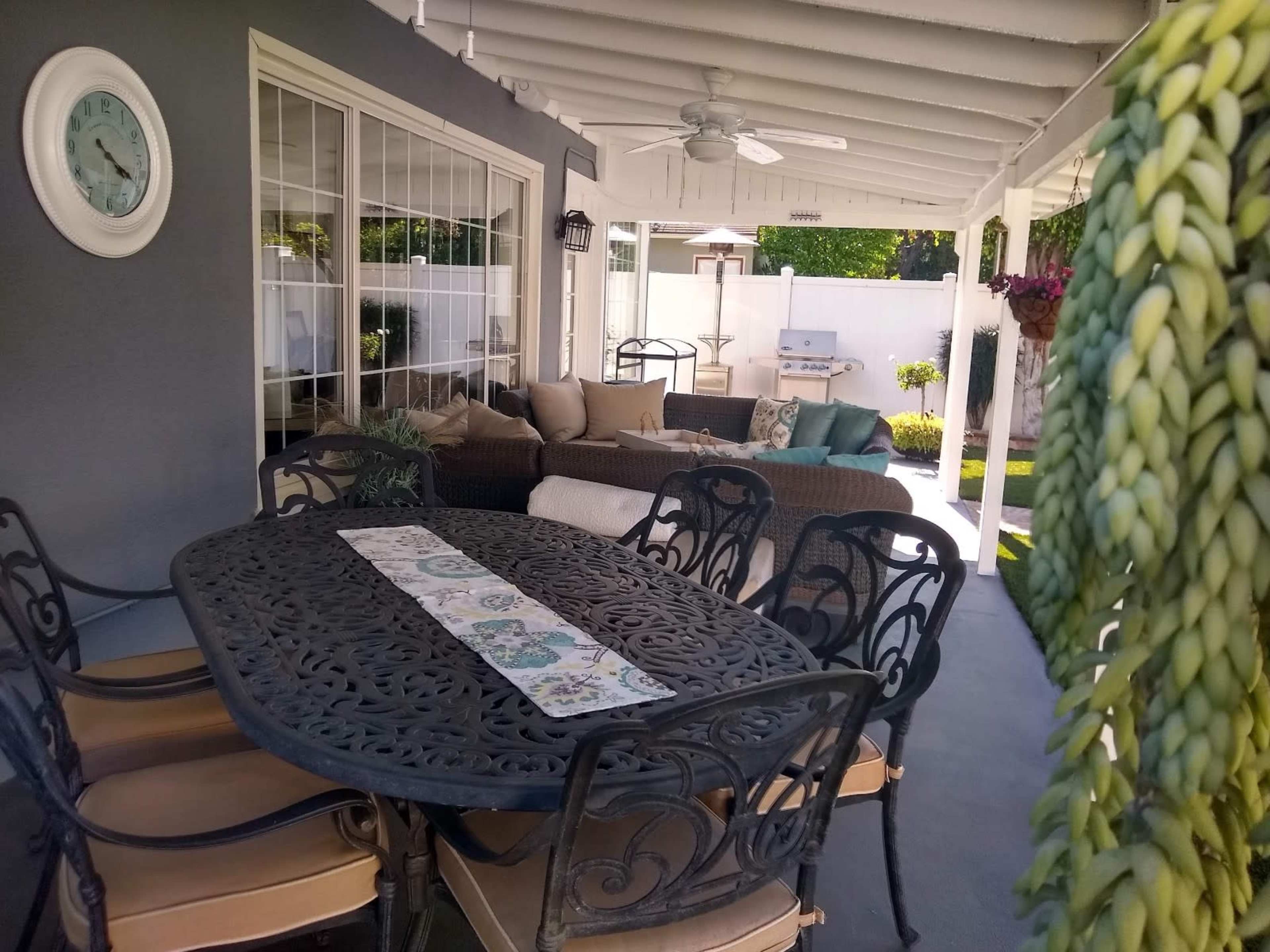 A patio area with a metal dining table and chairs, a seating arrangement with cushions, and various plants in a well-lit outdoor space.