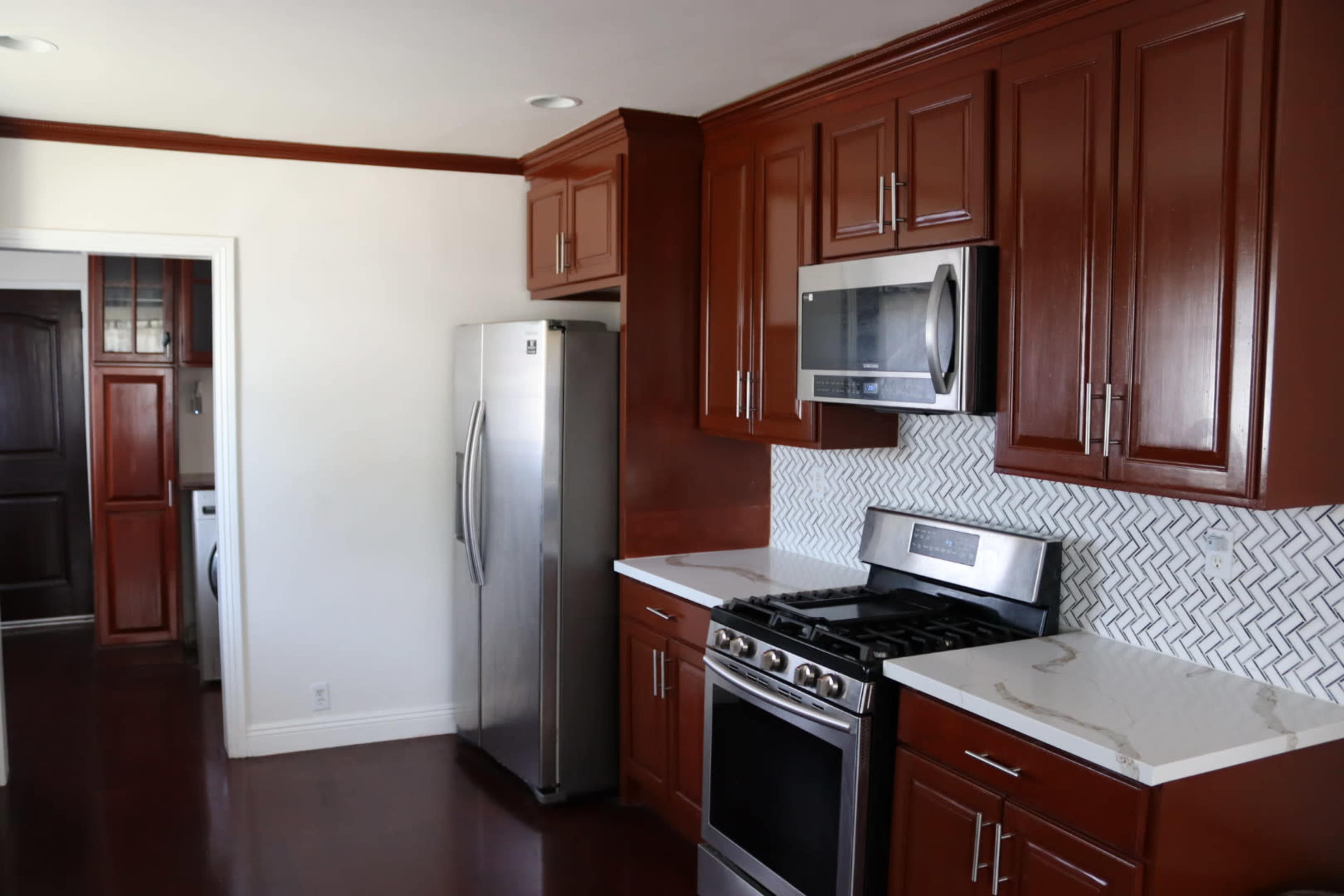 A modern kitchen with dark wood cabinetry, stainless steel appliances, and a tiled backsplash.