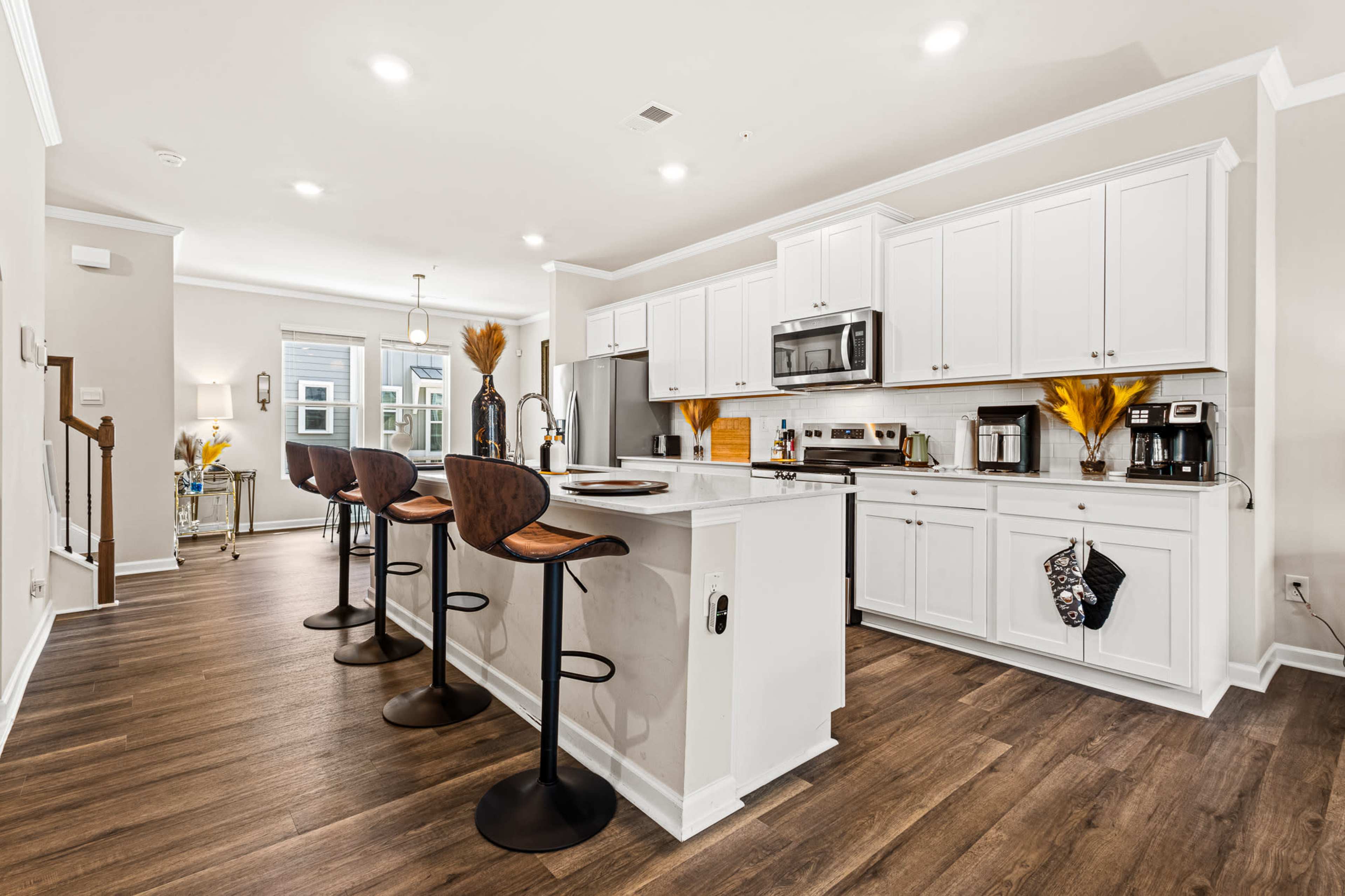 The image depicts a modern kitchen with white cabinets, stainless steel appliances, and a large island with bar stools.