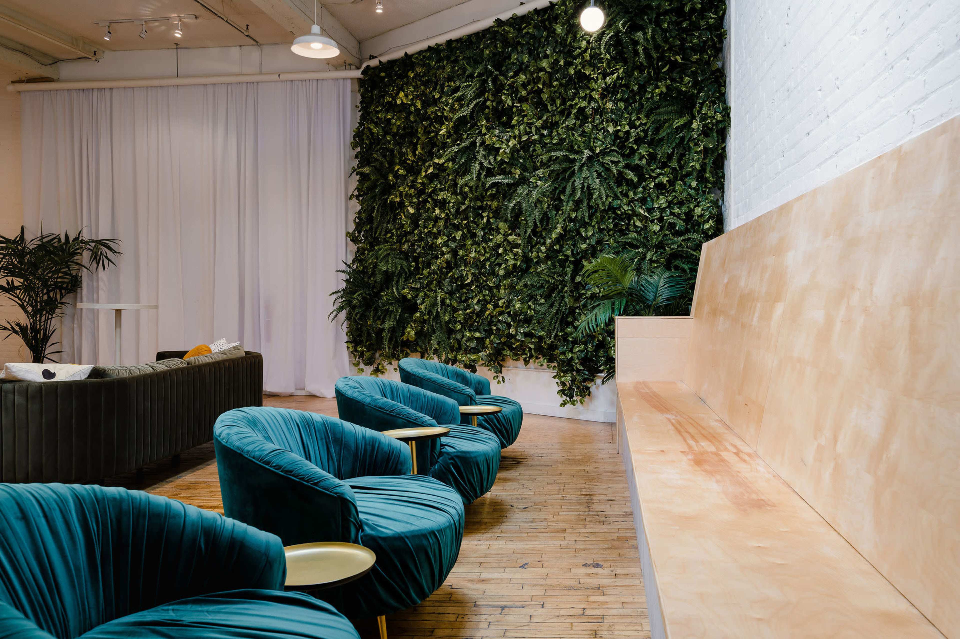 The image depicts a modern interior space featuring green velvet chairs, a wooden bench, and a vertical garden wall.