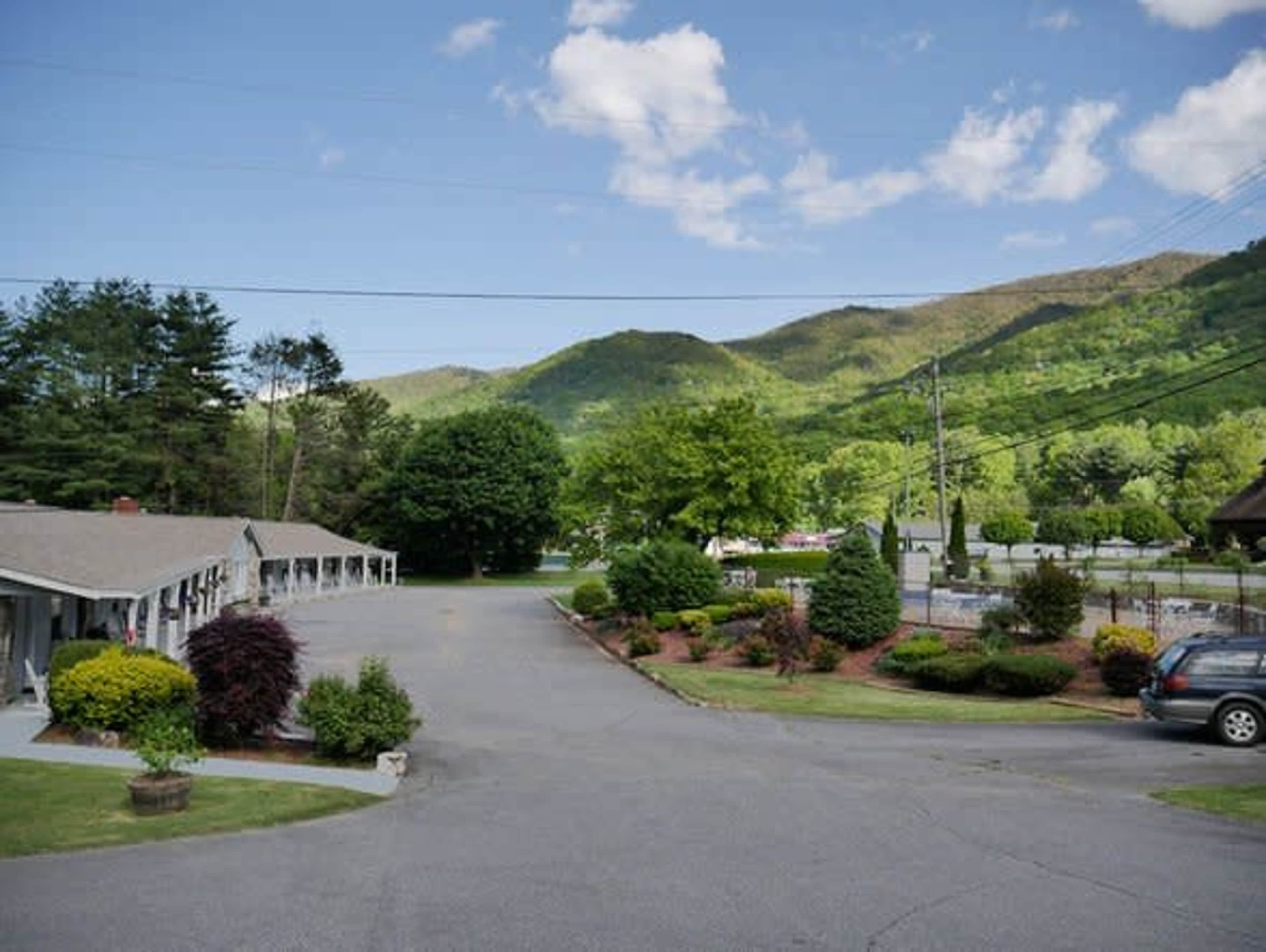 A roadside motel with a parking area and a view of green mountains and blue skies in the background.