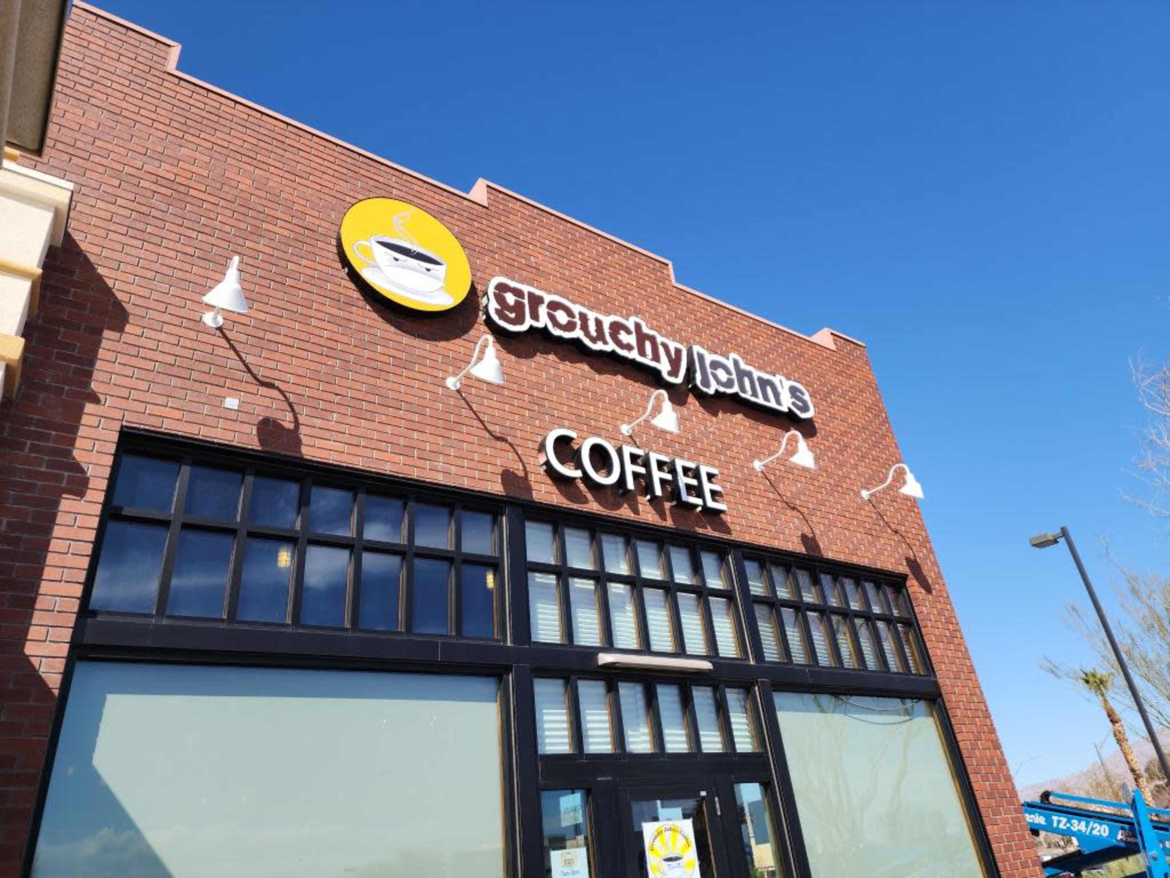 The exterior of a coffee shop called "Grouchy John's Coffee," featuring a brick facade and large windows.