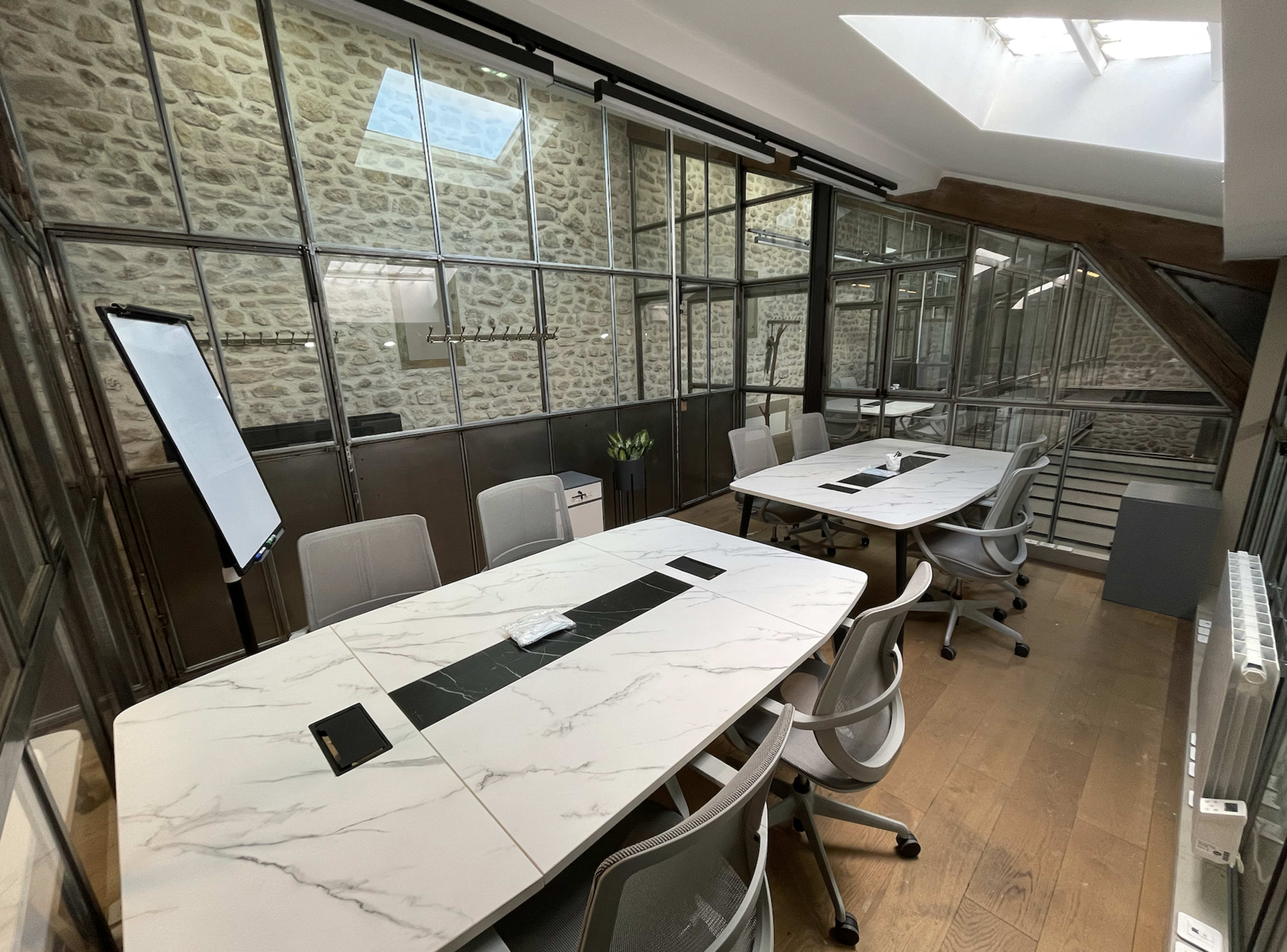 A modern conference room features glass walls, a large marble table, and ergonomic chairs, with natural light streaming through a skylight.