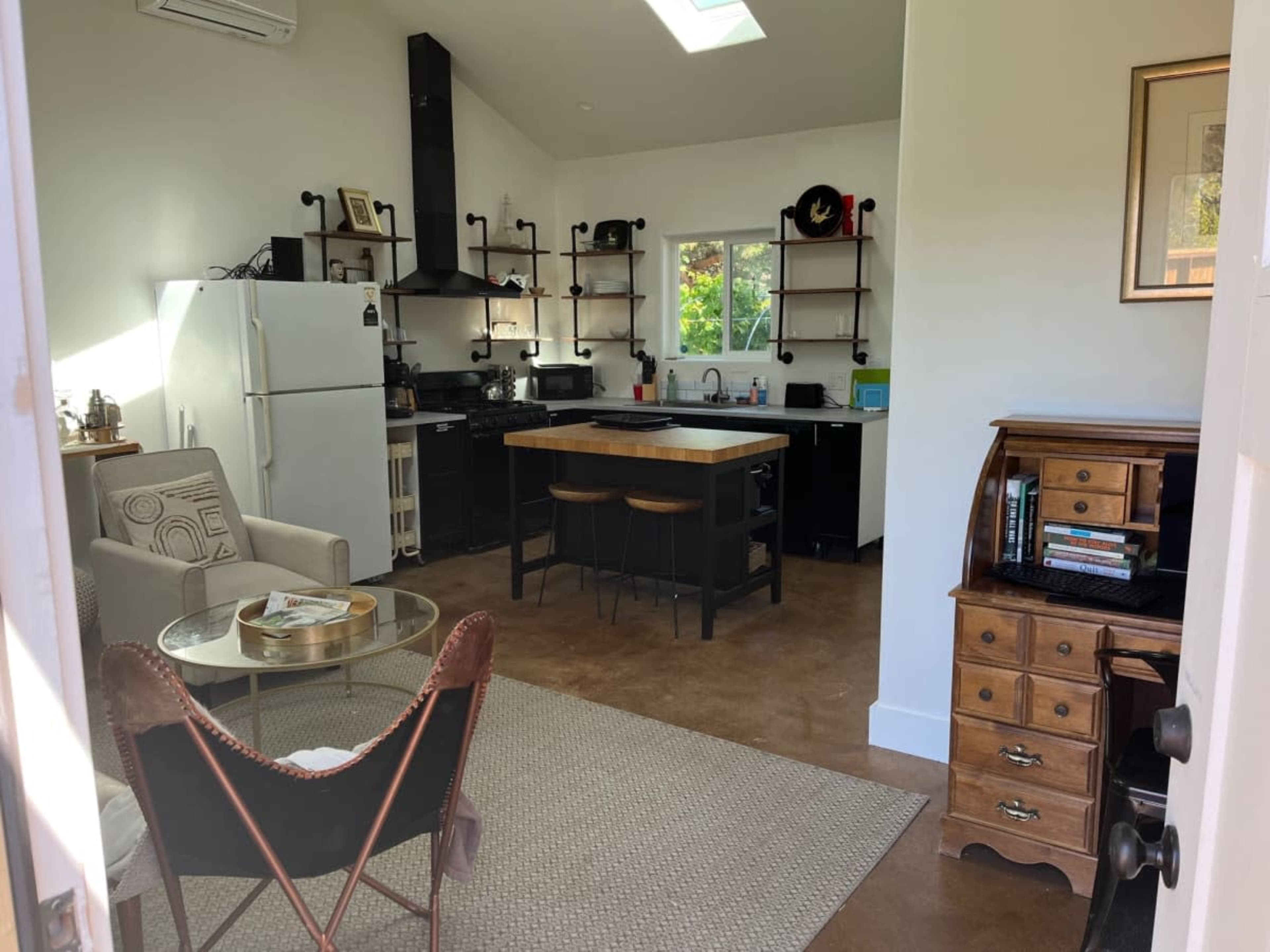 The image shows a modern kitchen and living area with a dining table, chairs, and various kitchen appliances, set against a backdrop of white walls and wood accents.
