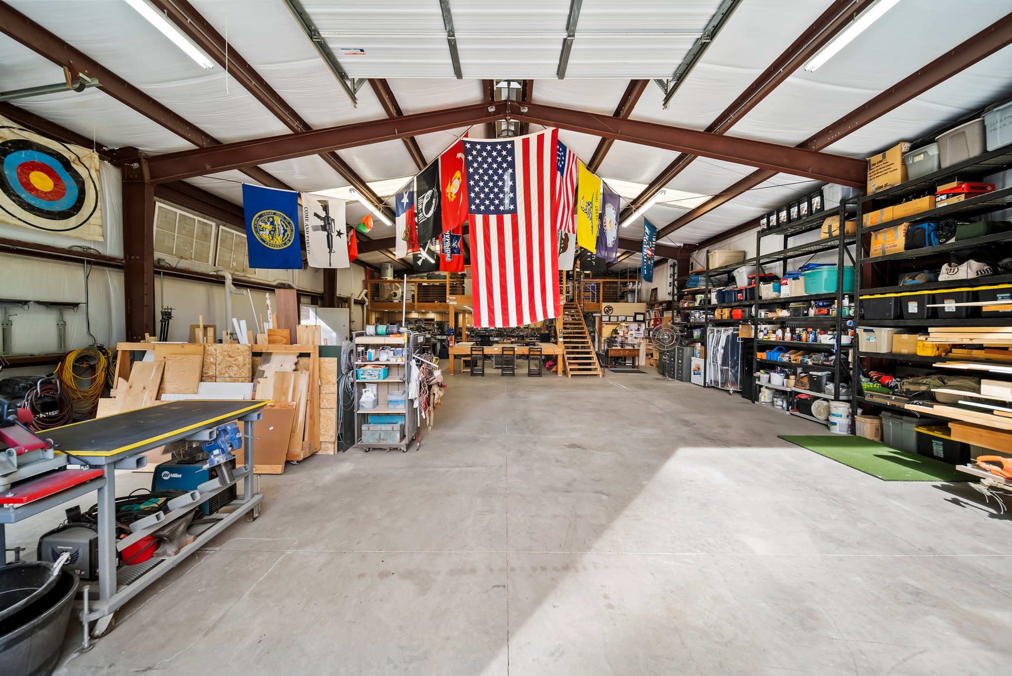 The image shows a spacious workshop with various tools, storage shelves, and flags hanging from the ceiling.