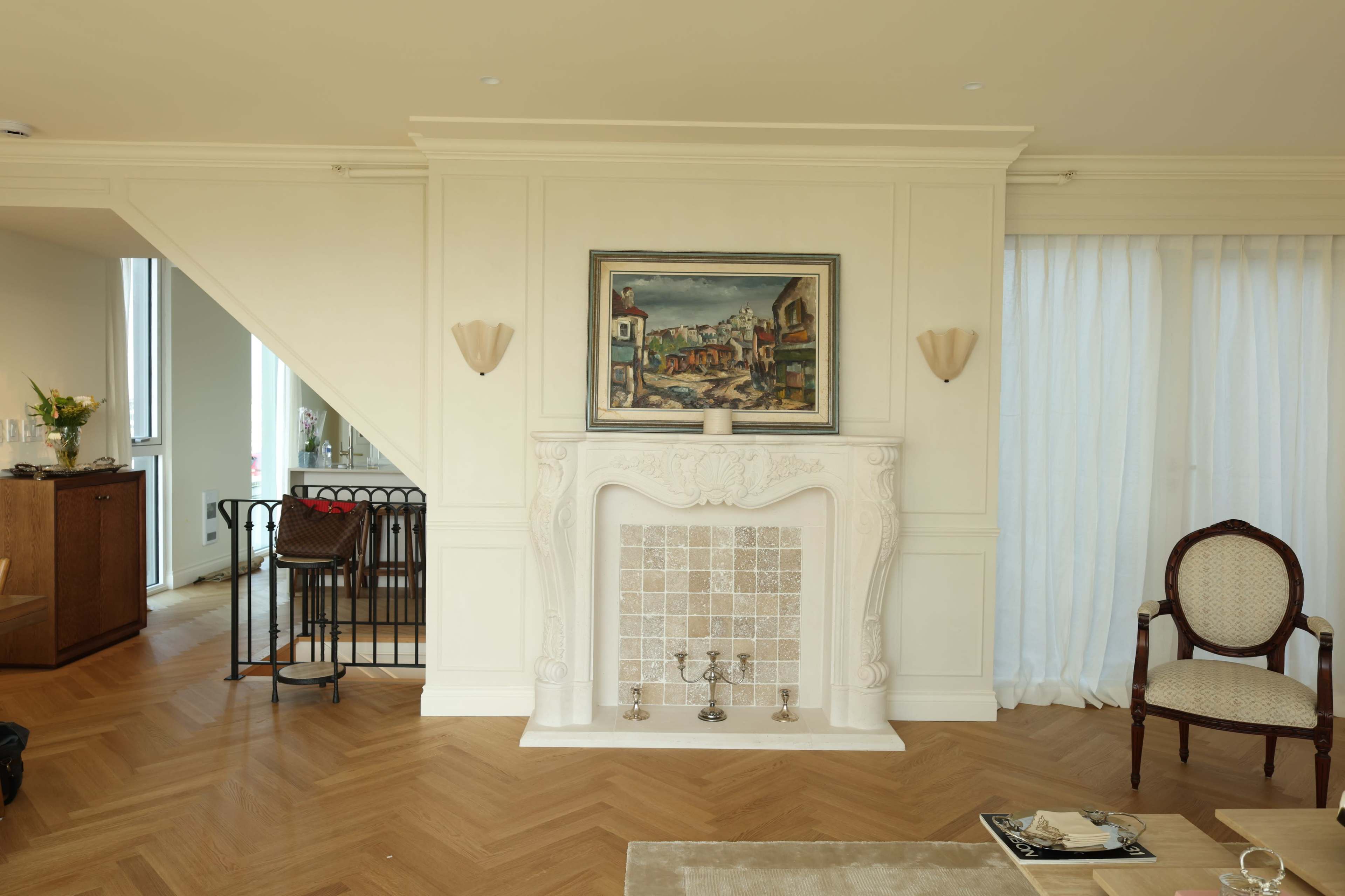 The image shows a modern living room featuring a decorative fireplace with a painting above it, hardwood flooring, and a mix of classic and contemporary furniture.