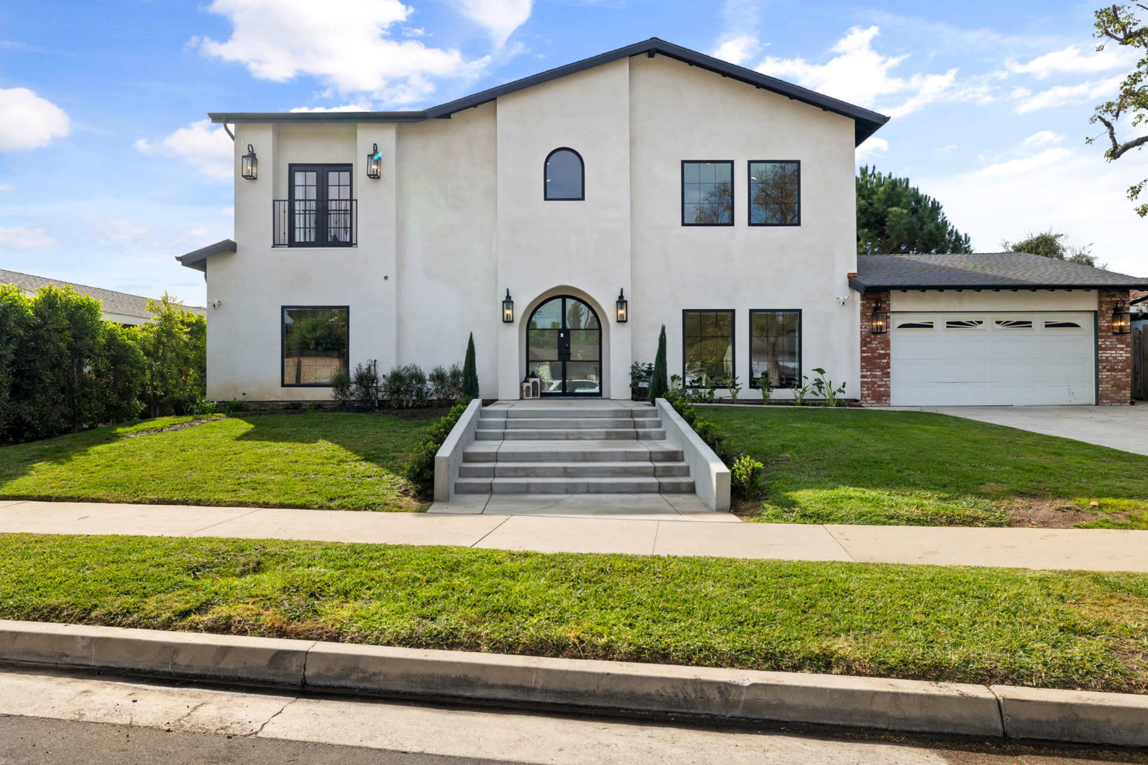 A large, two-story house with a modern design features a central archway entrance, large windows, and a manicured lawn.