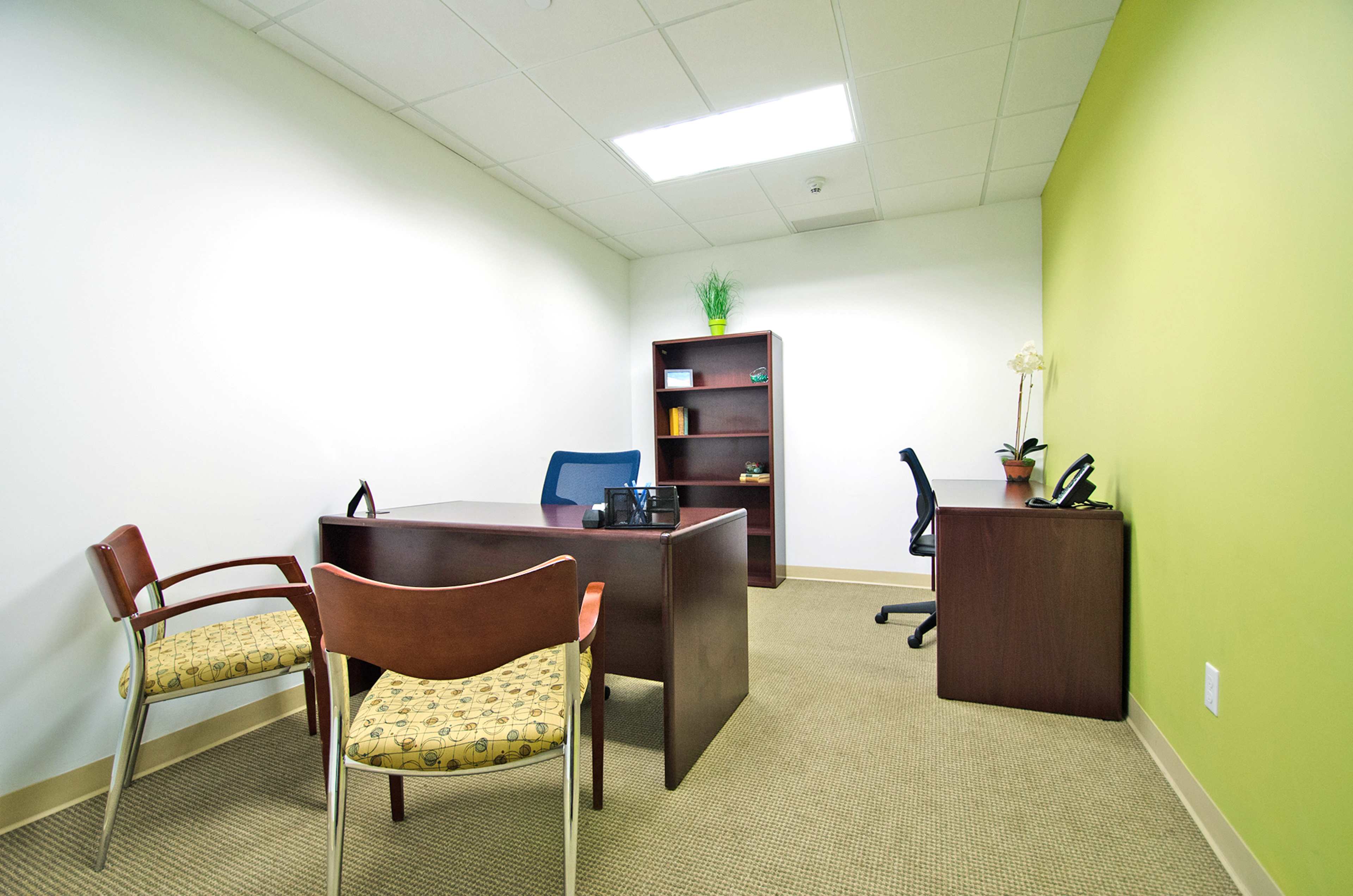 A small, brightly-lit office with a desk, two chairs, a bookshelf, and a phone.