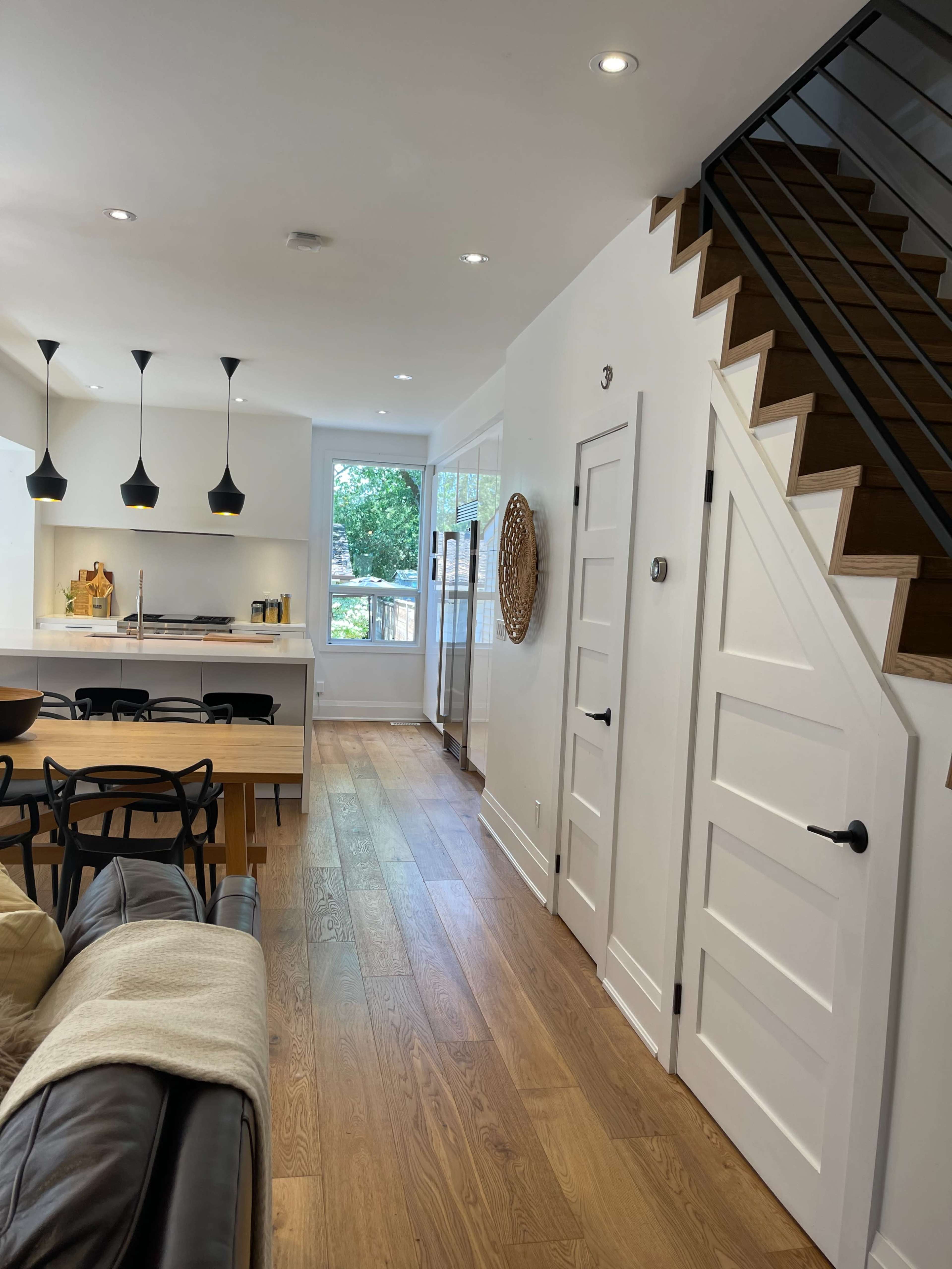 A modern interior space featuring a living area with a leather sofa, a dining table, and a staircase leading to an upper level.