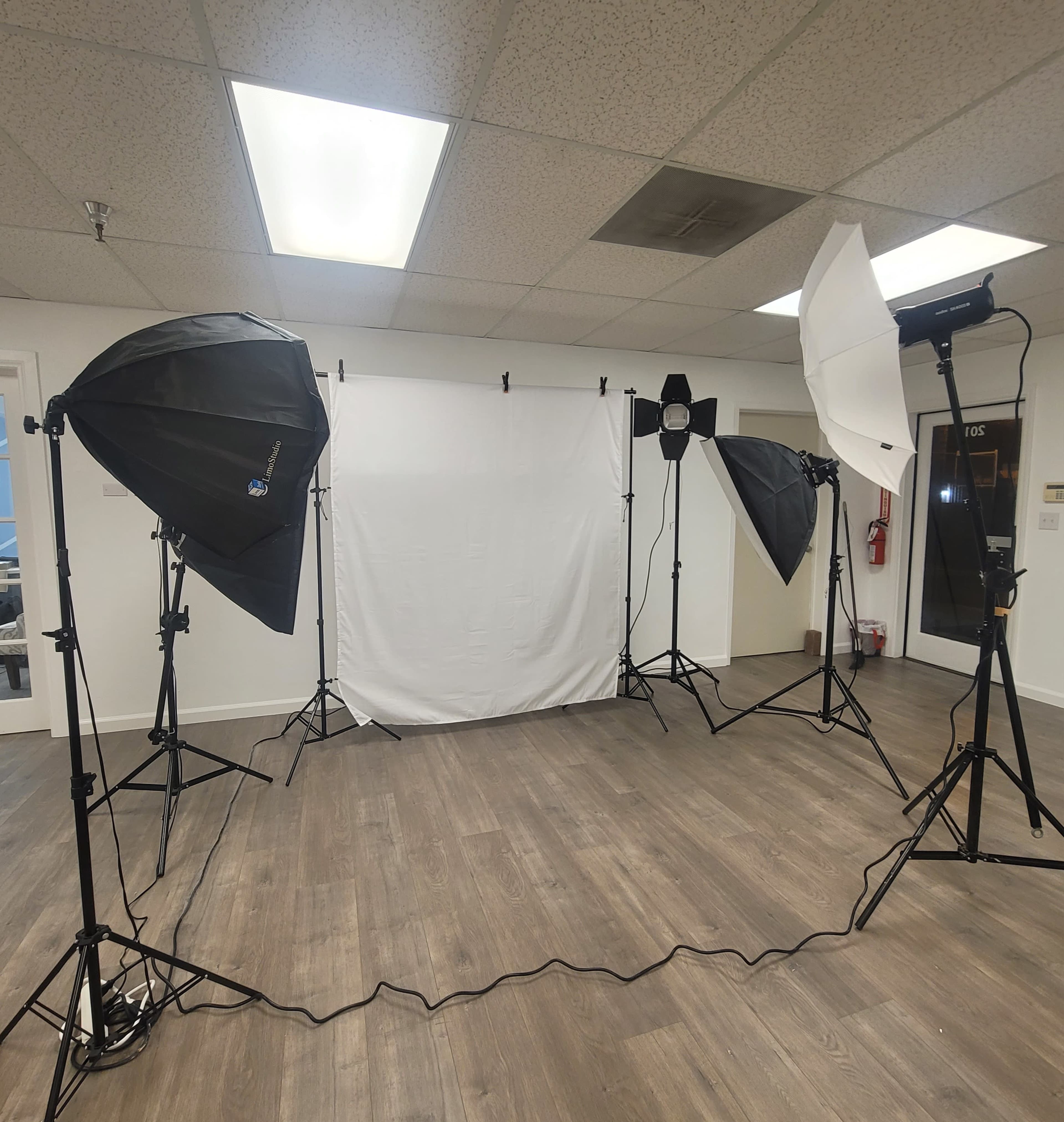 The image shows a photography studio setup with several softboxes, a light stand, and a backdrop on a wooden floor.