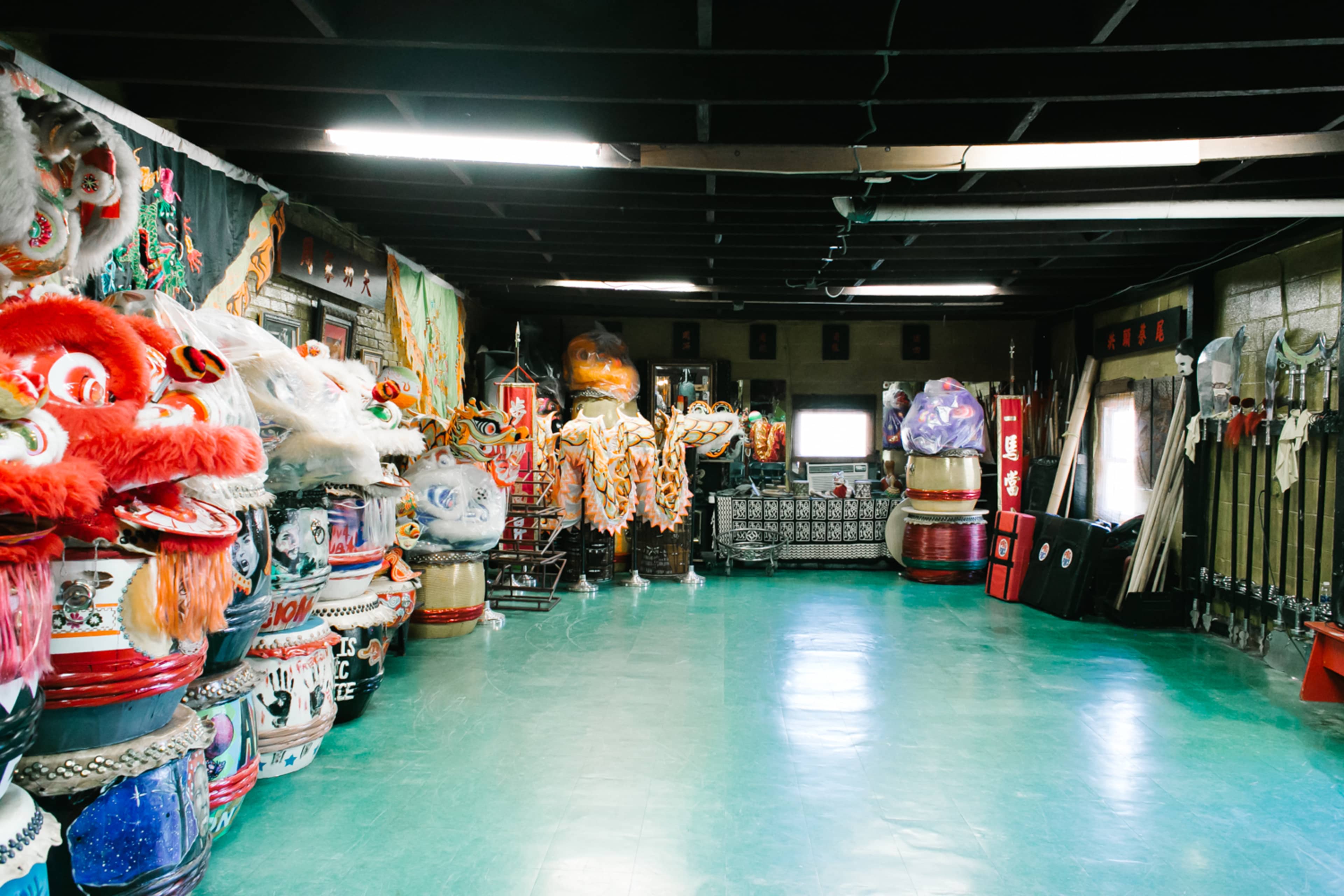 A spacious room filled with colorful traditional costumes, large lion dance heads, and various props lined along the walls.
