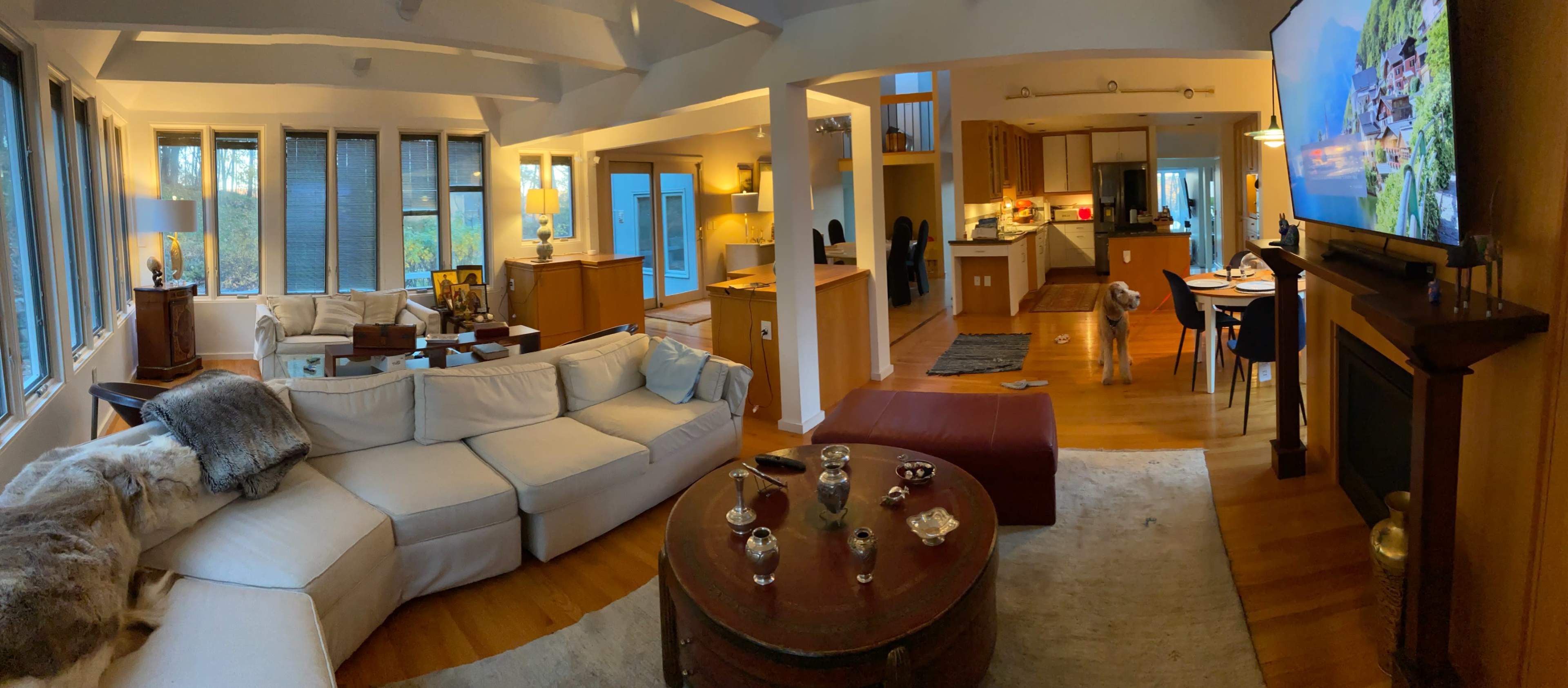 The image shows a spacious and modern living area with a sectional sofa, a coffee table, and a view of the kitchen and dining area in the background.