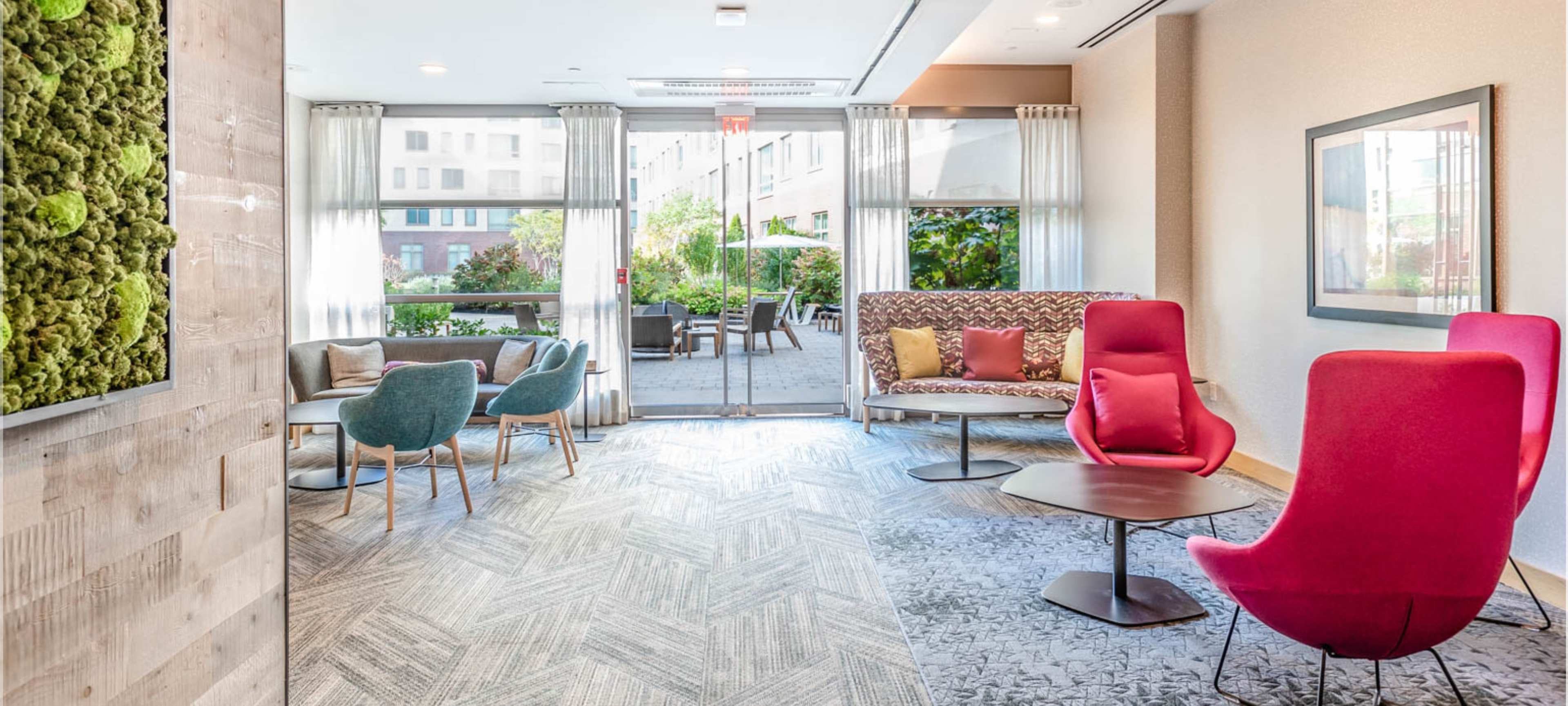 A modern seating area with colorful chairs, a sofa, and large windows overlooking a garden.