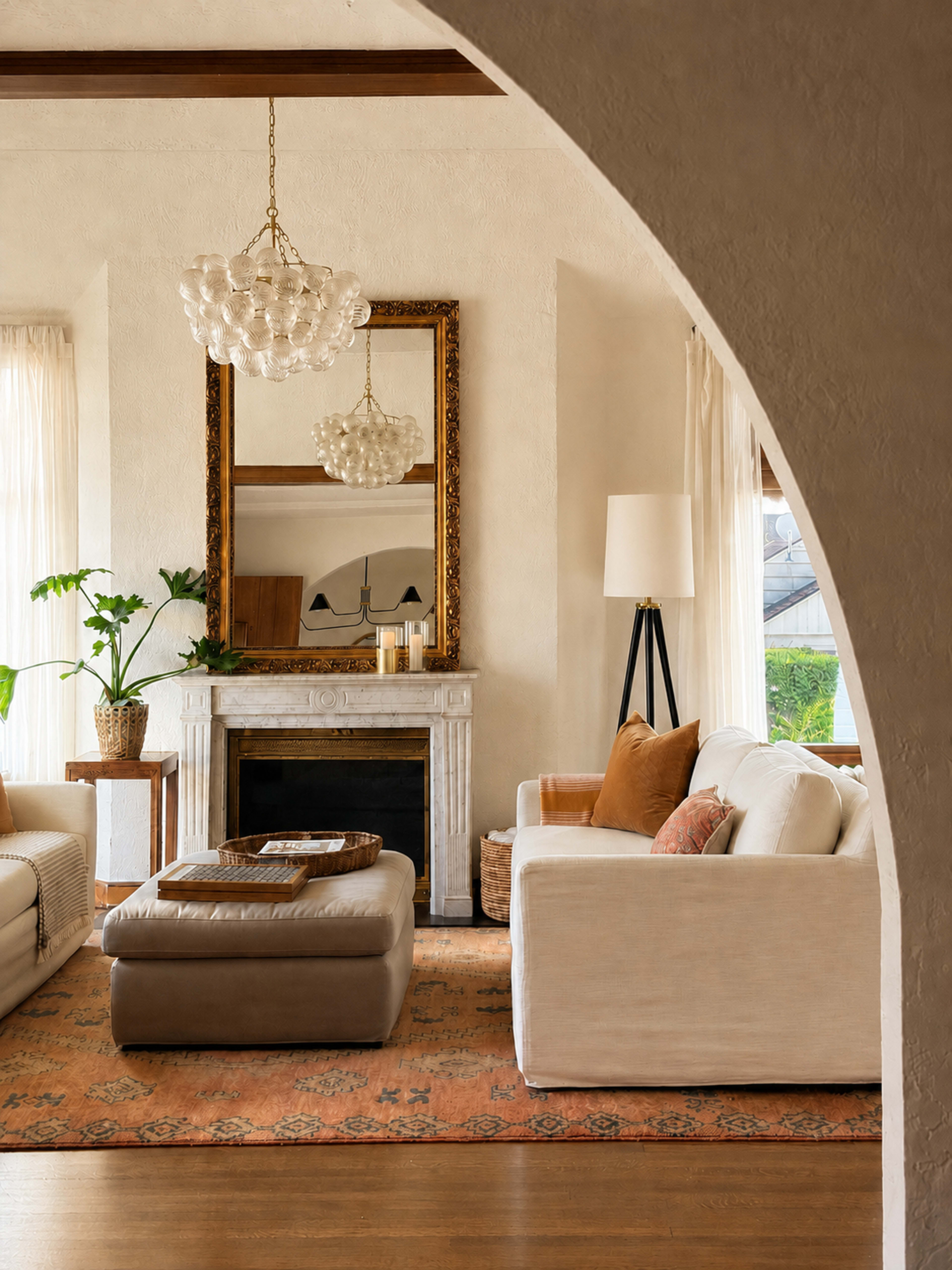 The image shows a cozy living room with a fireplace, a large mirror, and comfortable seating arranged around a central ottoman on a decorative rug.