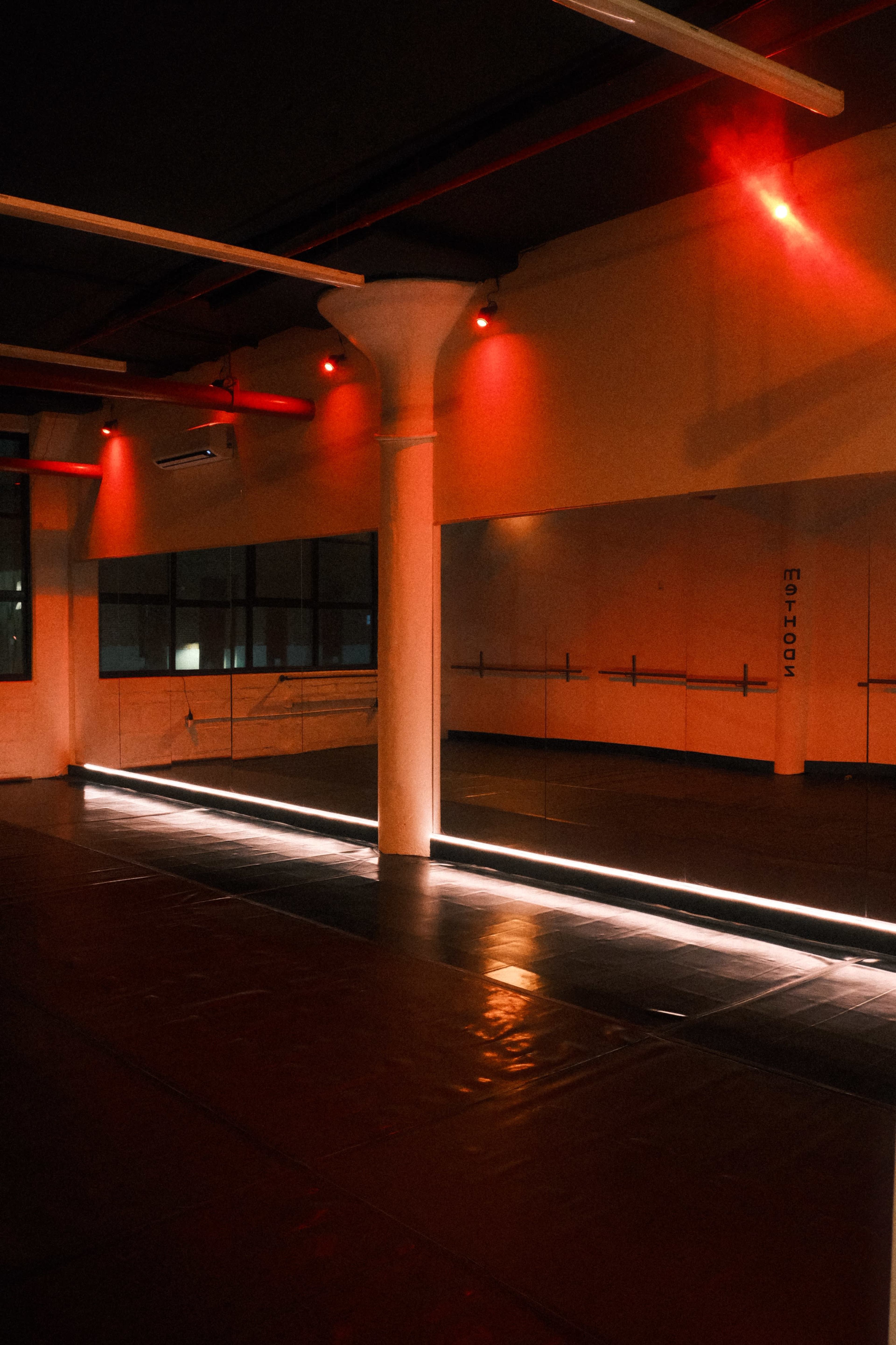 The image shows a dimly lit dance studio with red lighting and mirrors along one wall.