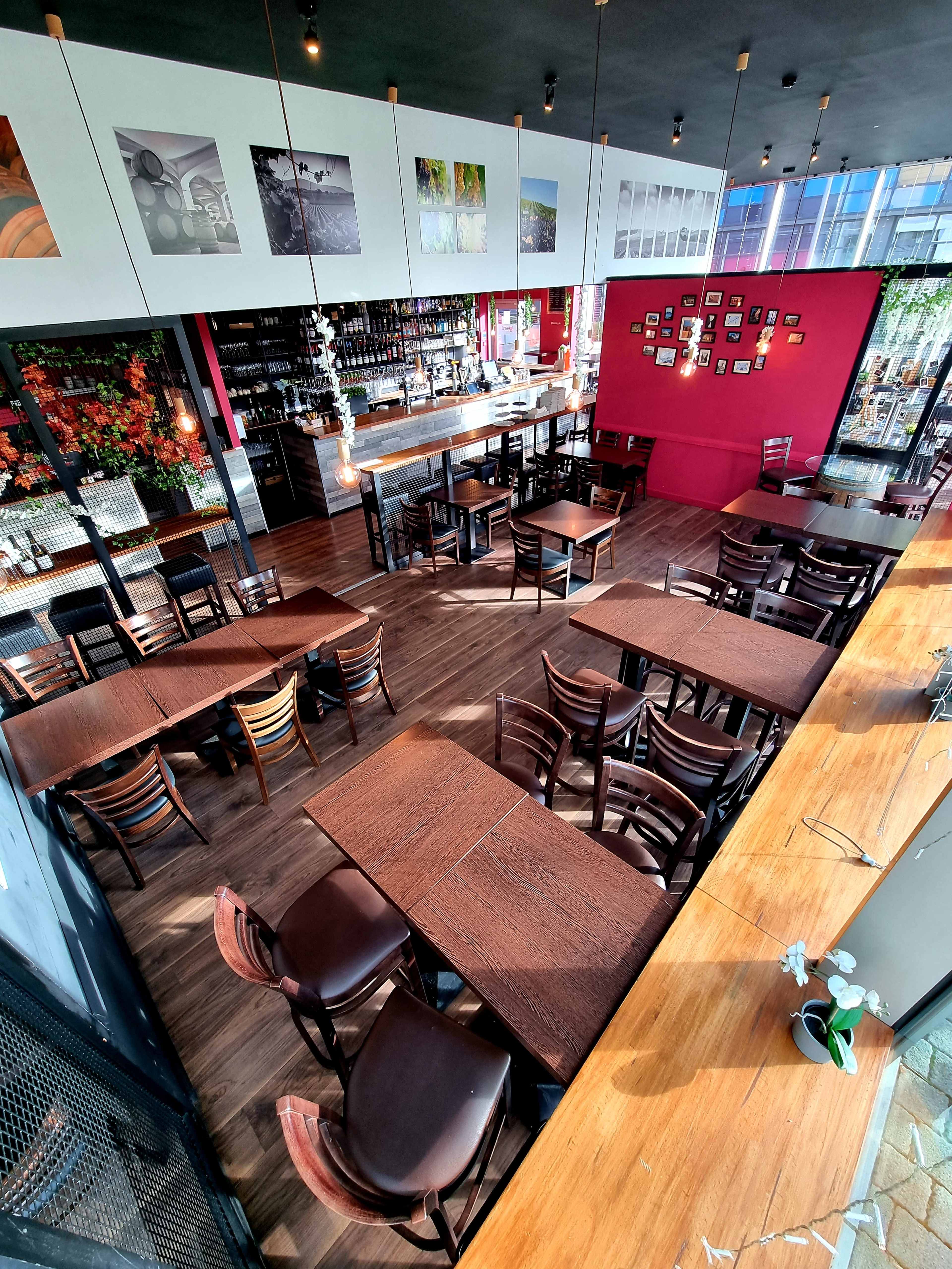 A modern café interior with wooden tables and chairs arranged throughout, featuring a bar area and decorative wall art.