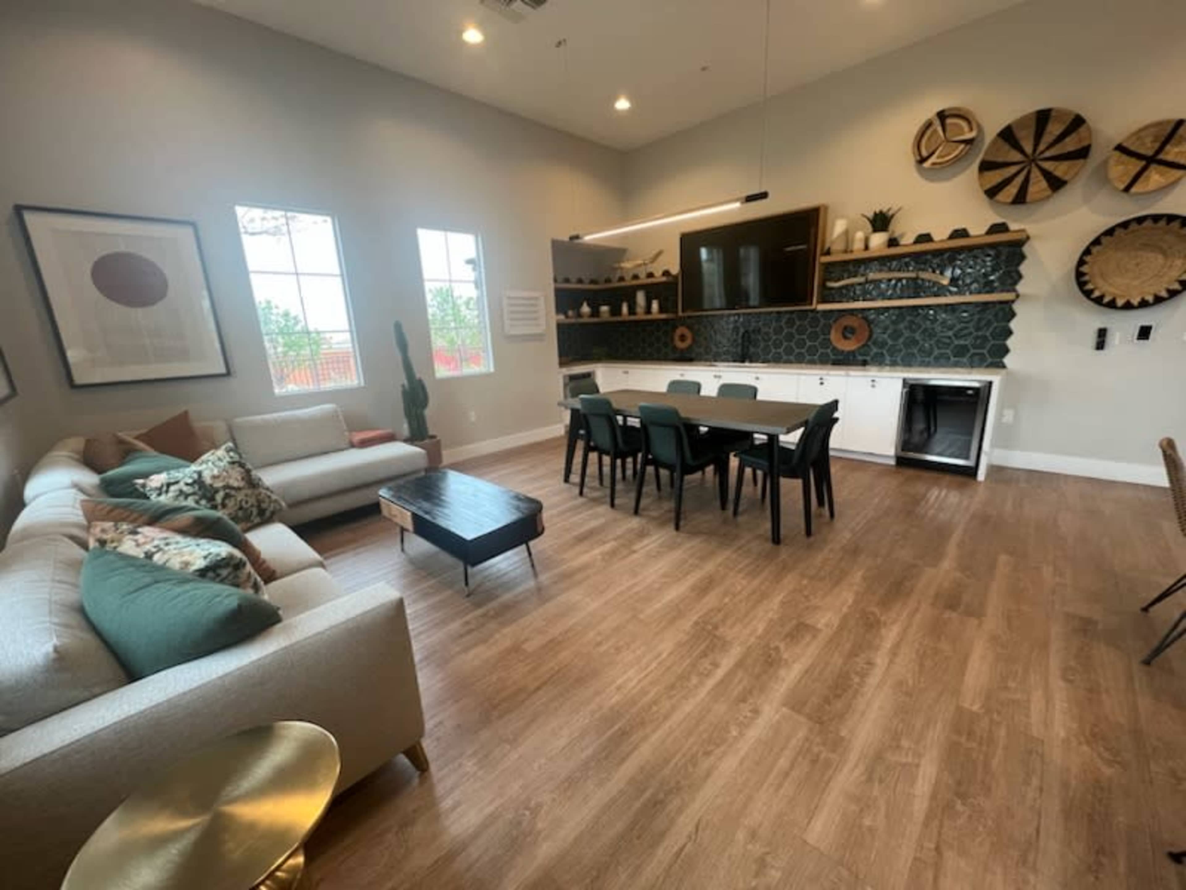 A spacious room with a seating area featuring a light-colored sofa, a dining table with black chairs, and decorative wall plates arranged above a dark wall unit.