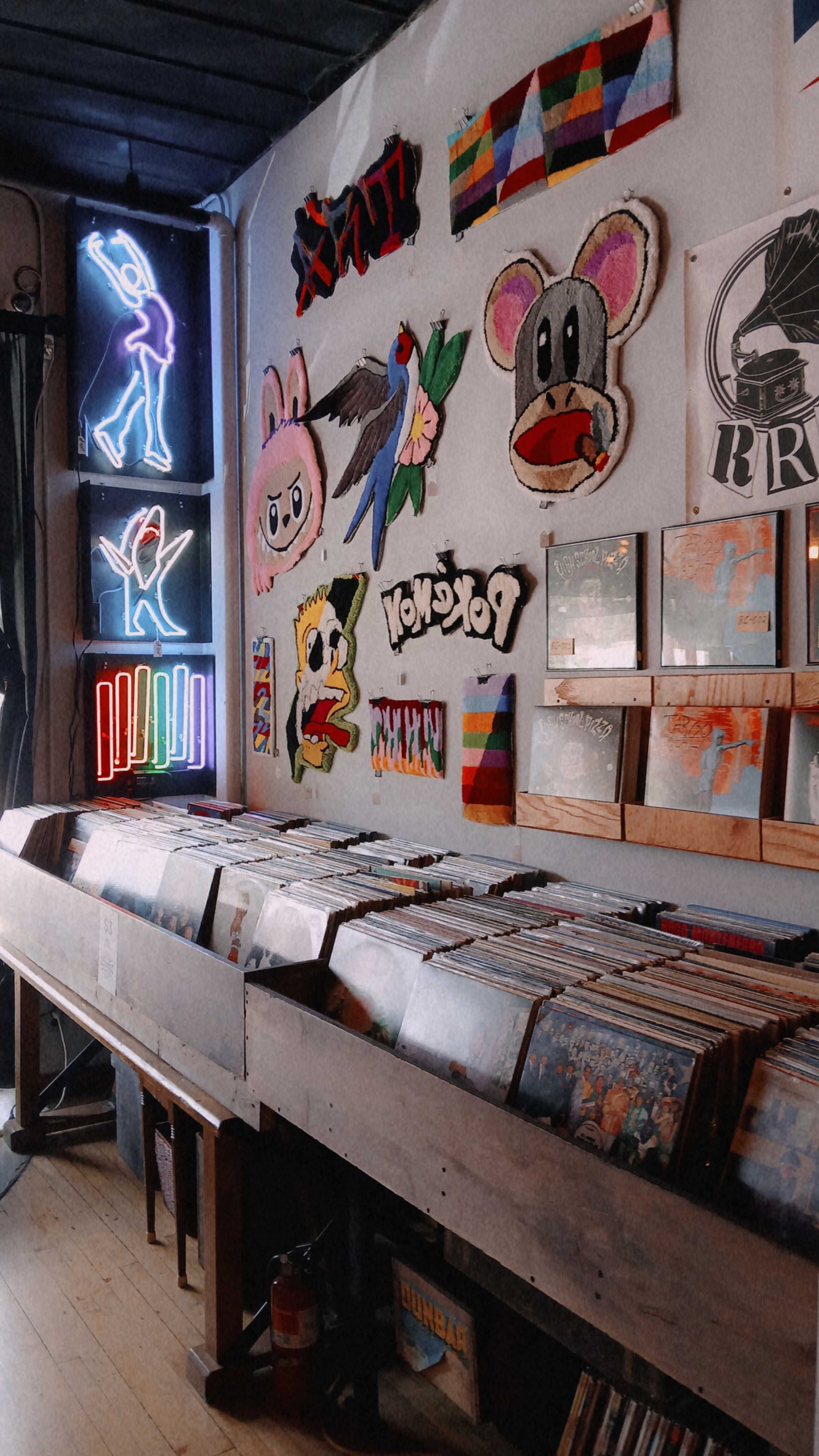 A wooden display holds various vinyl records beneath colorful art and neon signs on the wall.