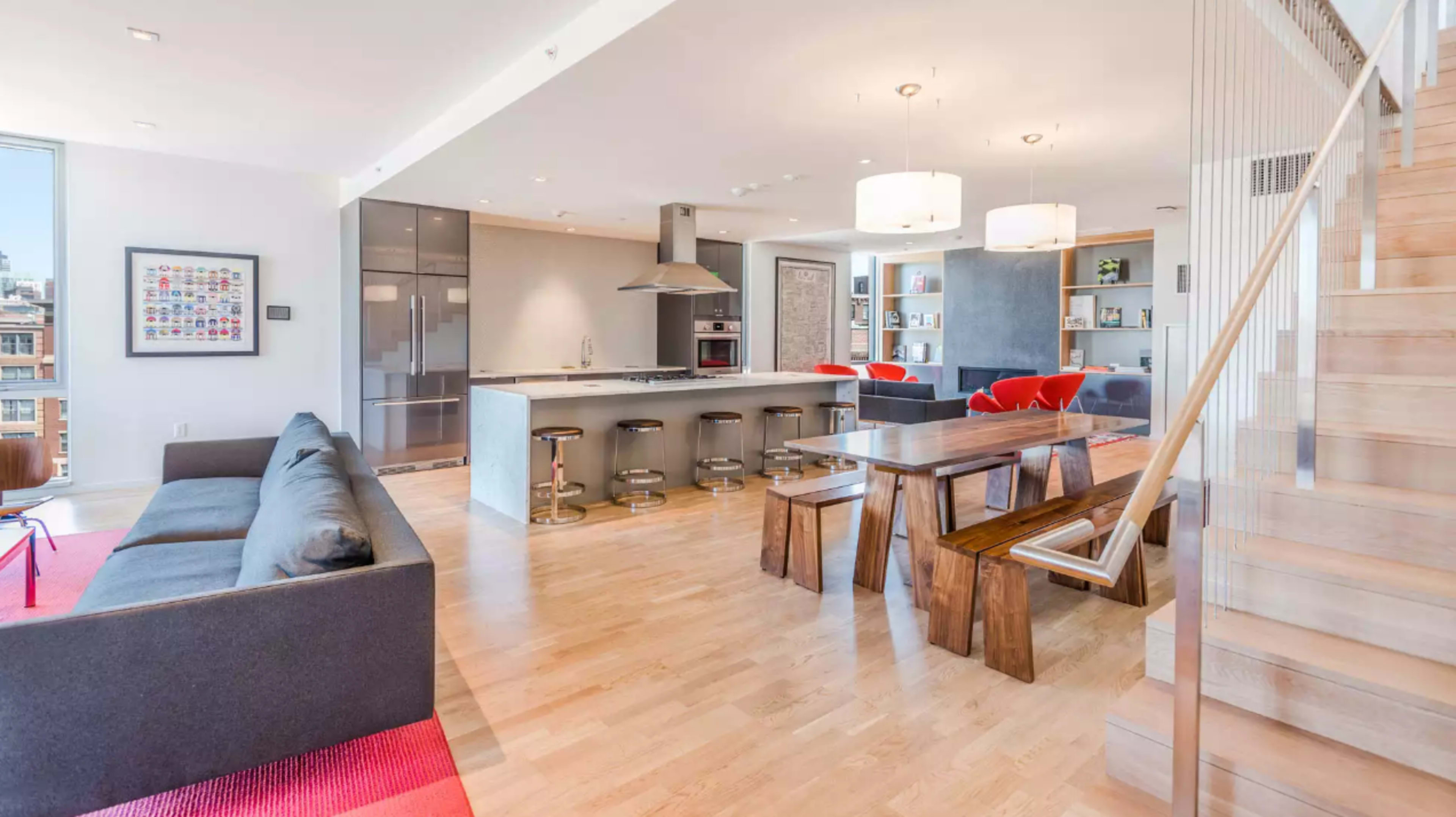 A modern open-concept living space featuring a kitchen with a large island, a dining table made of wood, and a staircase leading to an upper level.