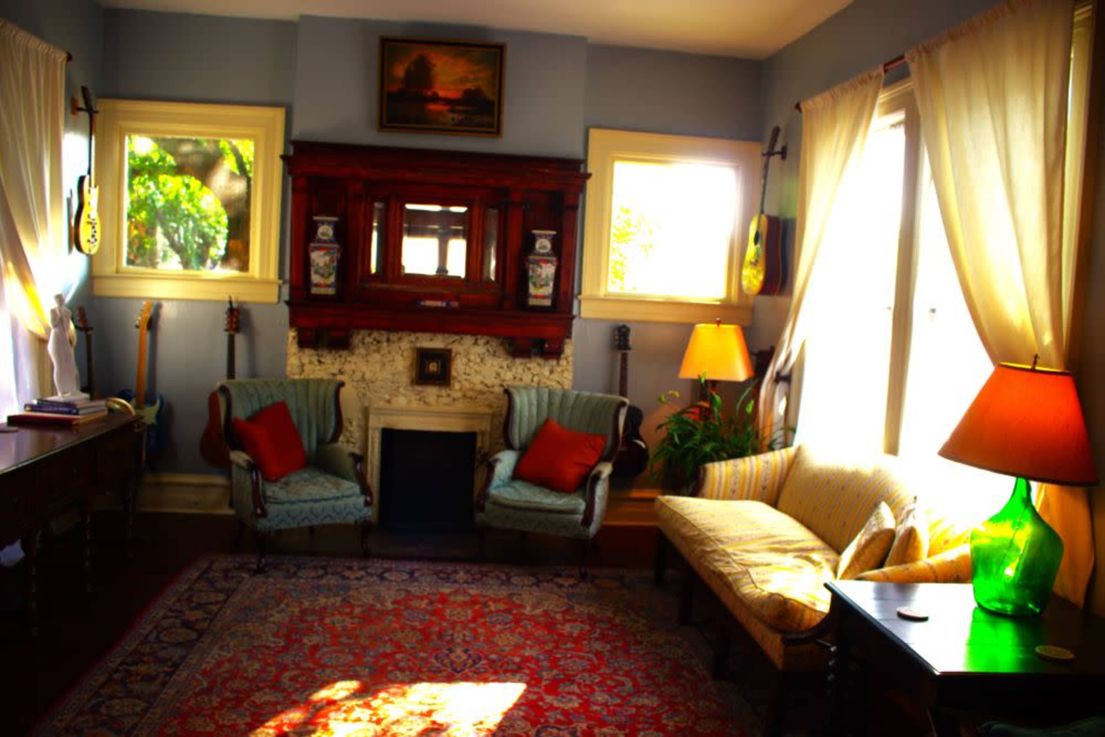 A cozy living room features two armchairs, a sofa, a fireplace with decorative elements, and large windows allowing natural light to fill the space.