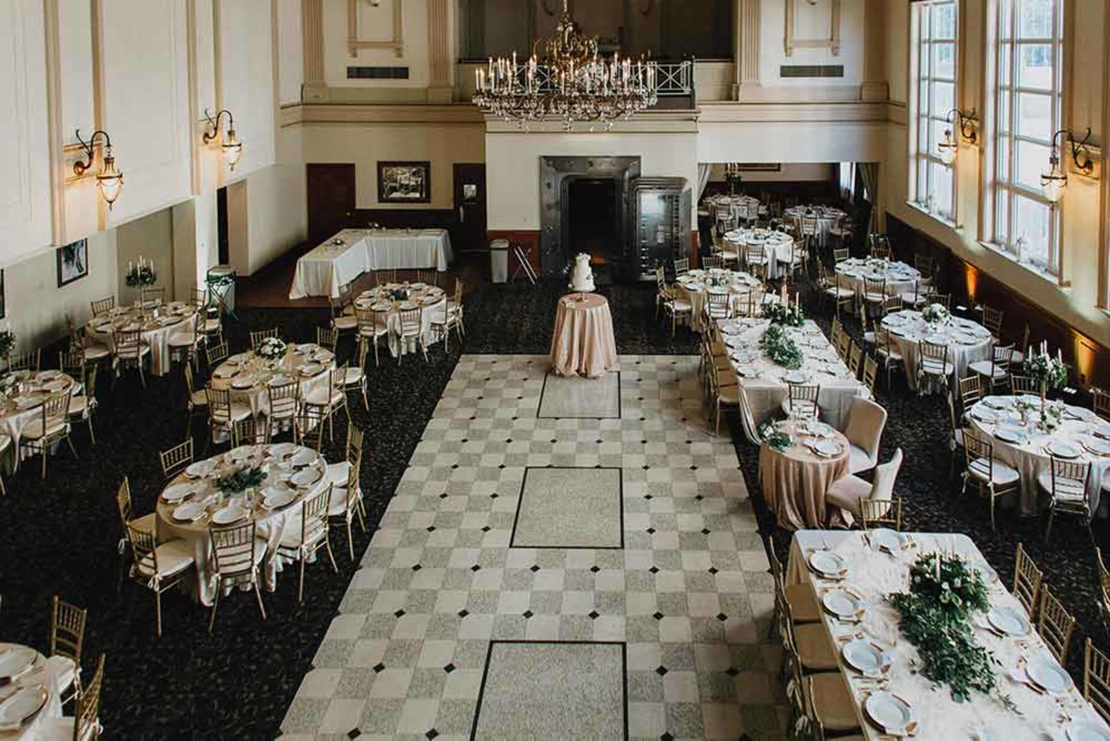 A banquet hall arranged with neatly set tables and a central cake display under a chandelier.