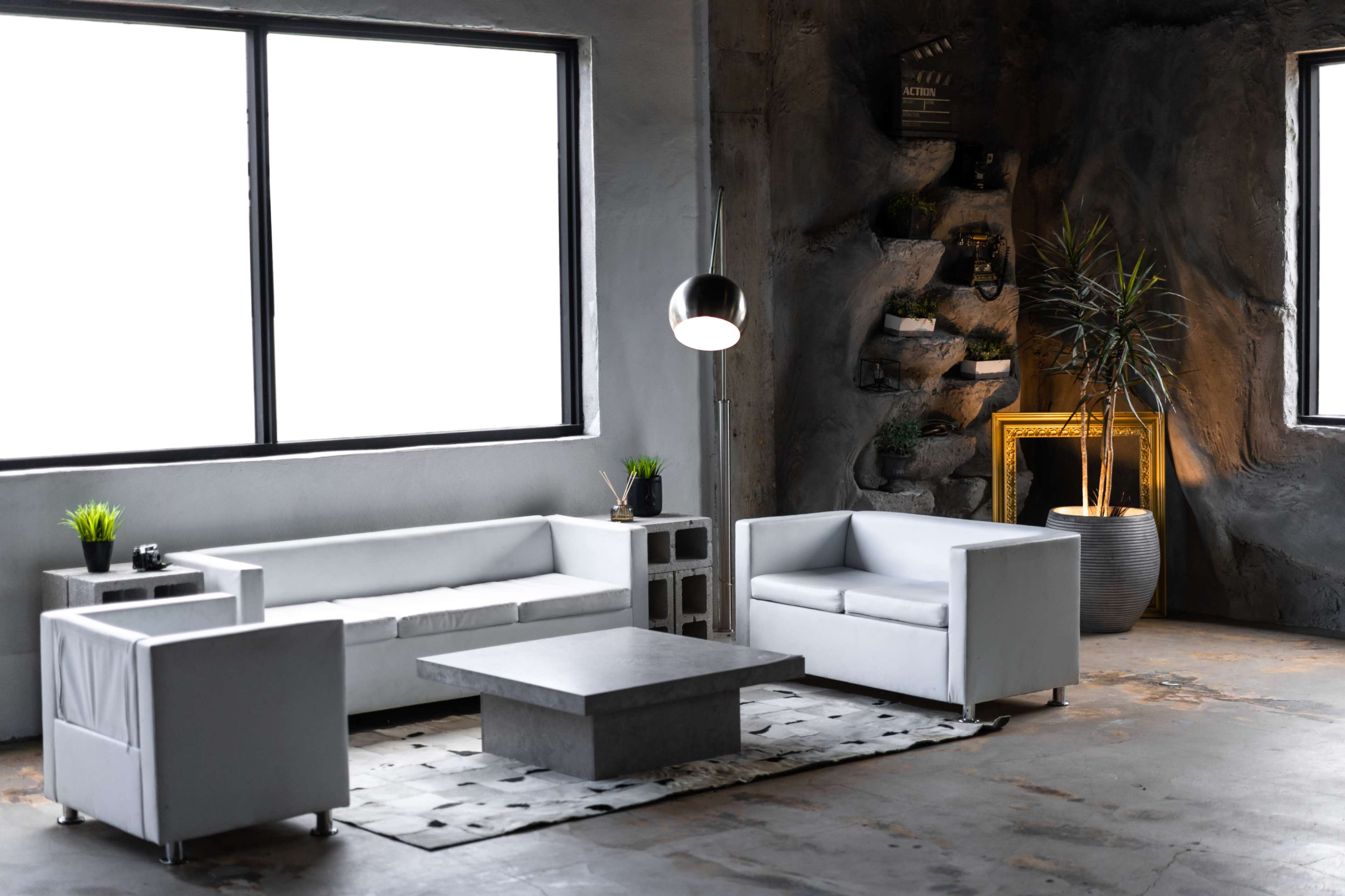 The image shows a modern interior living space featuring white leather sofas, a gray coffee table, a large window, and decorative plants.