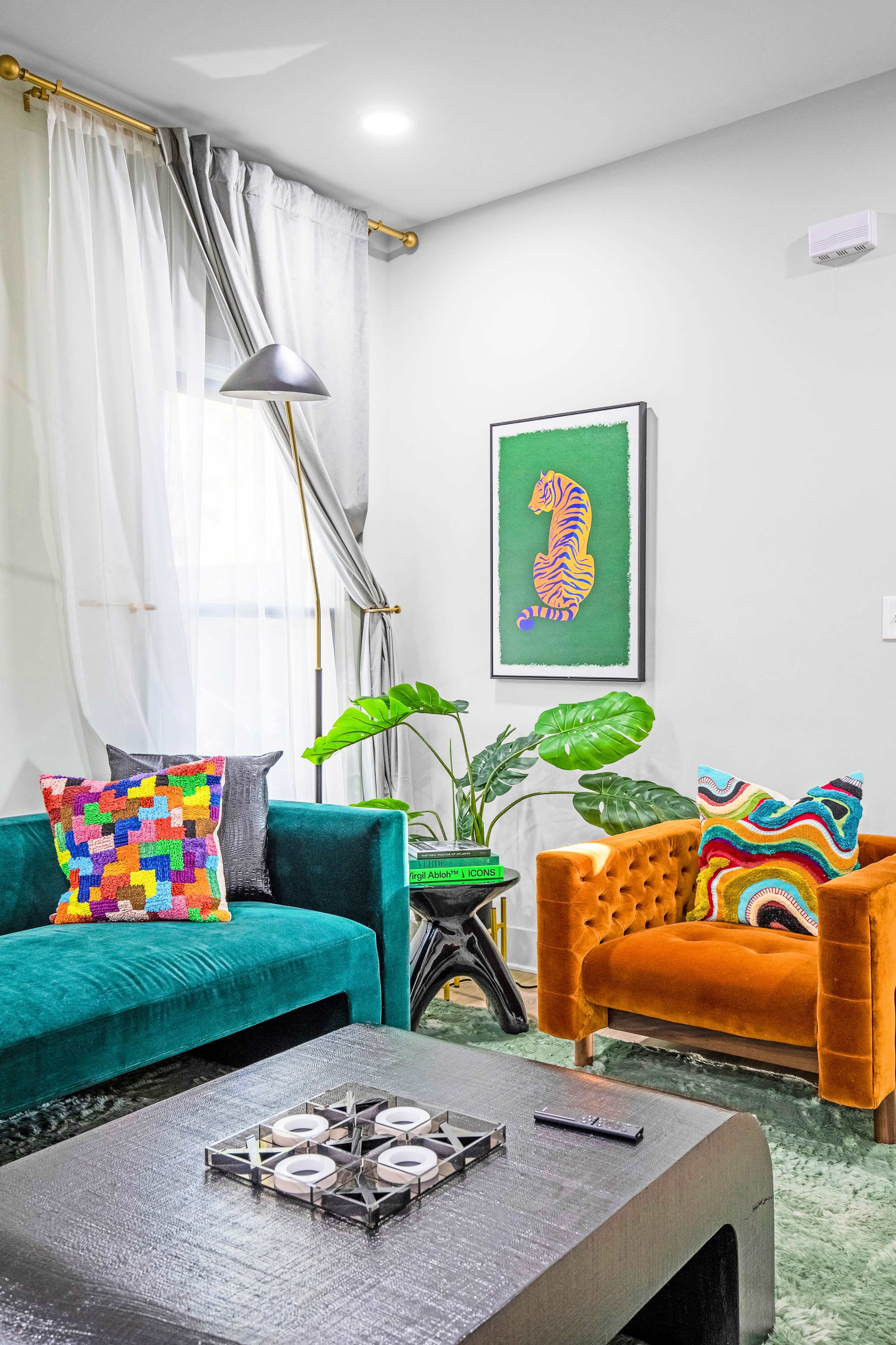 The scene features a brightly decorated living room with a green velvet sofa, an orange armchair, a patterned pillow, a coffee table, and artwork of a tiger on the wall, surrounded by potted plants.