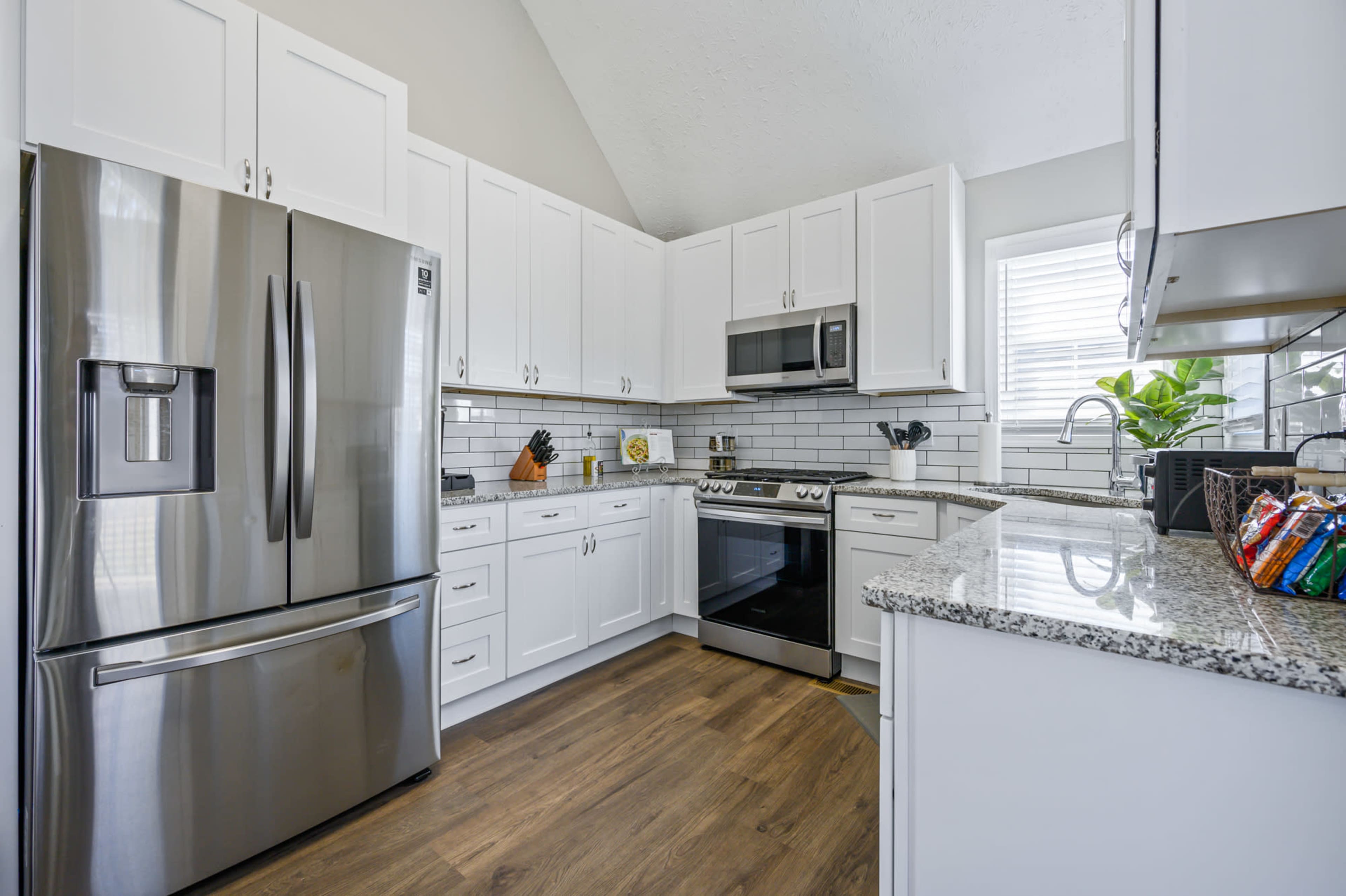 A modern kitchen features stainless steel appliances, white cabinetry, and a granite countertop with a wood floor.