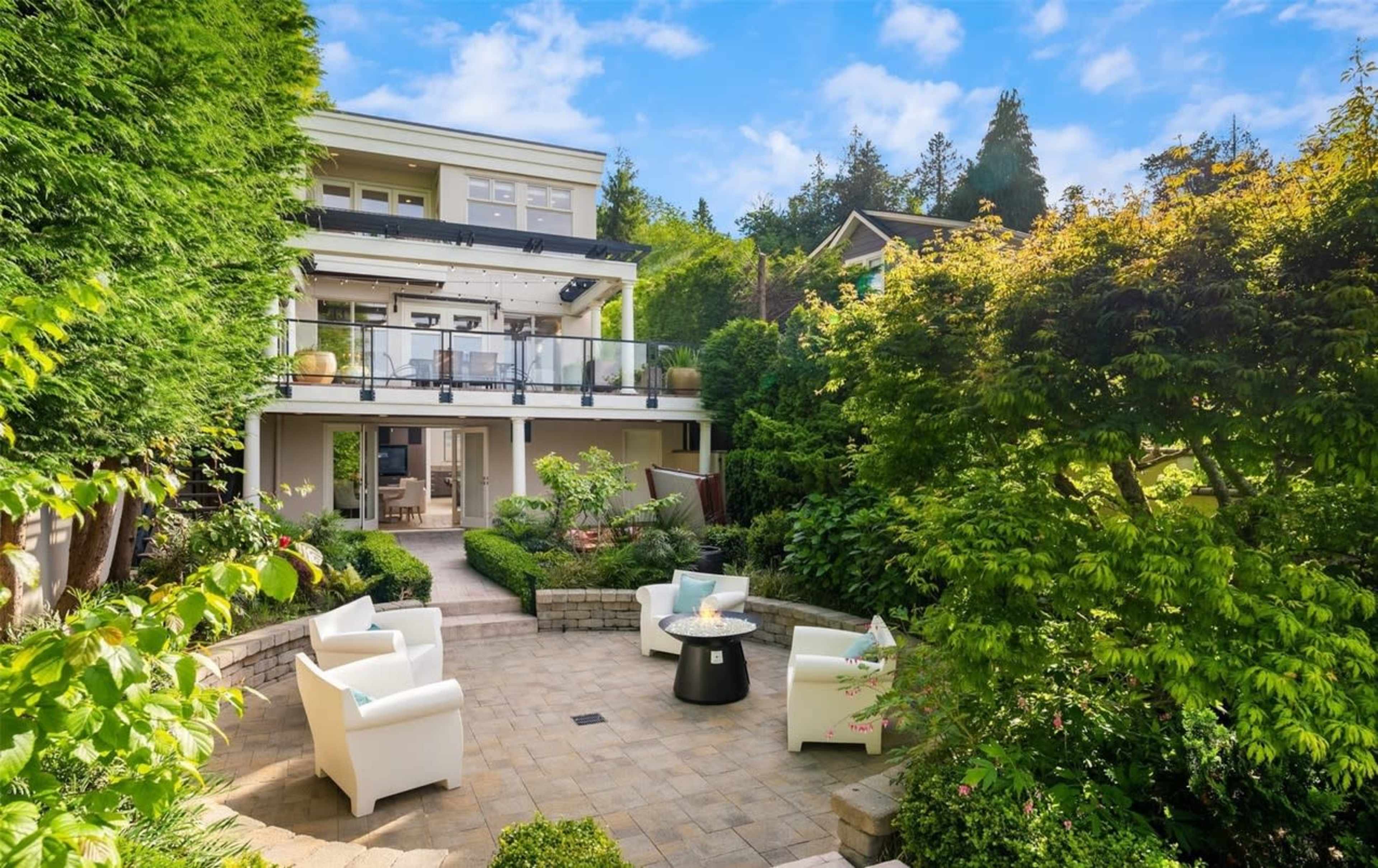 A multi-level house with a patio surrounded by lush greenery and modern outdoor furniture.