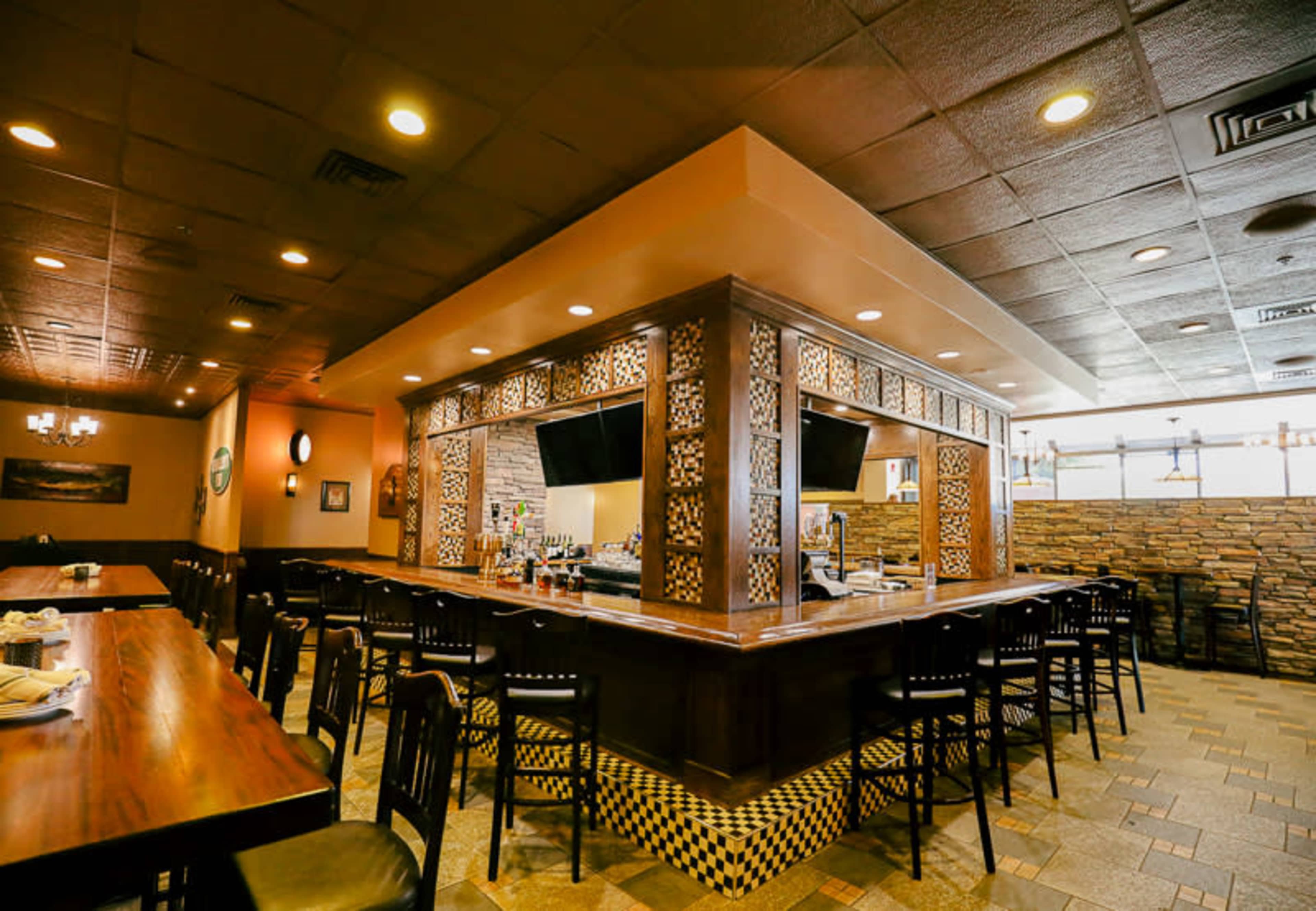 The interior of a restaurant featuring a centrally located bar with decorative woodwork and surrounding seating areas.