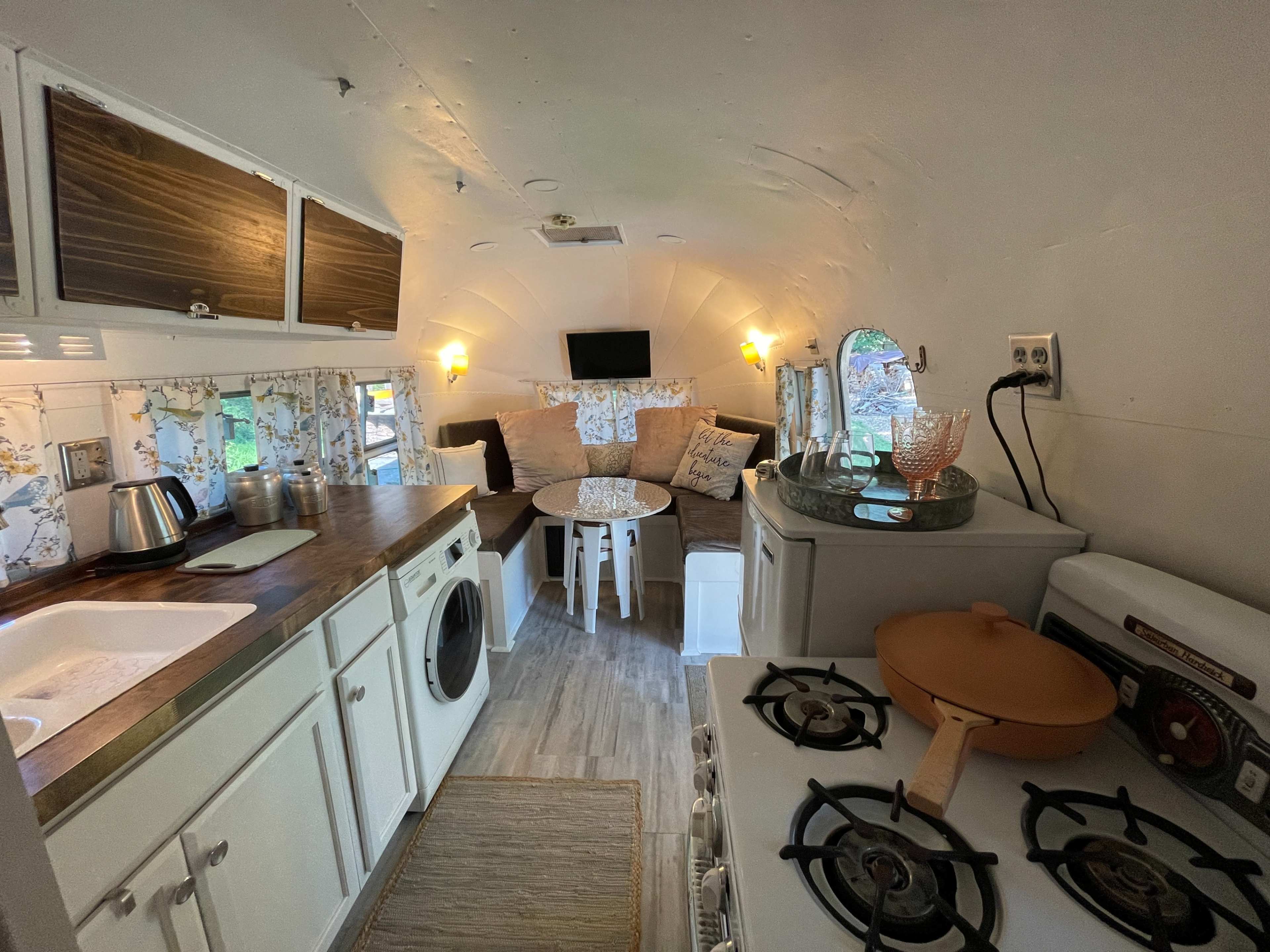 The interior of a converted vintage trailer with a kitchenette, a cozy seating area, and decorative elements.