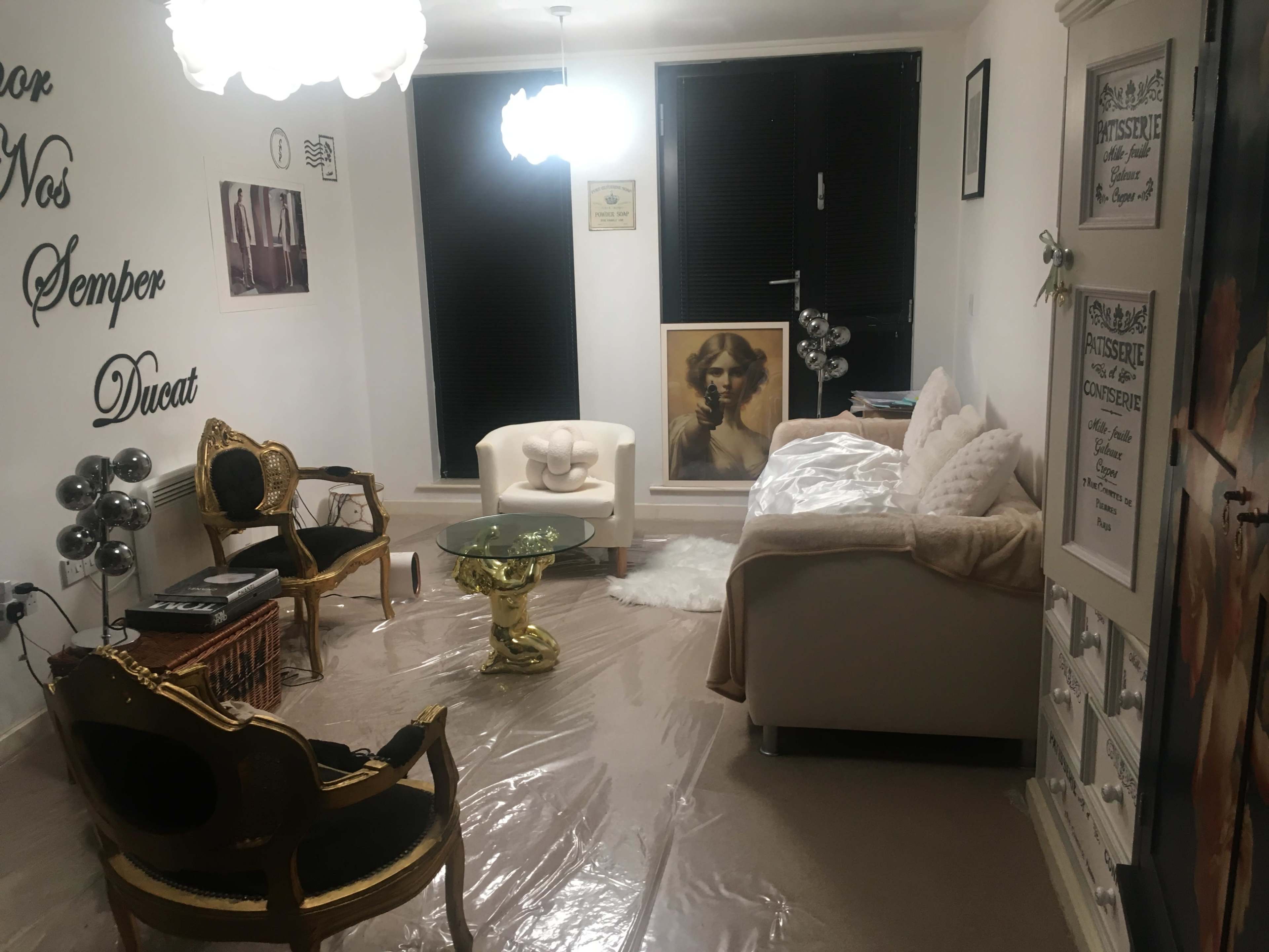 The image shows a living room with a white couch, a golden coffee table, black and gold chairs, and decorative artwork on the walls.