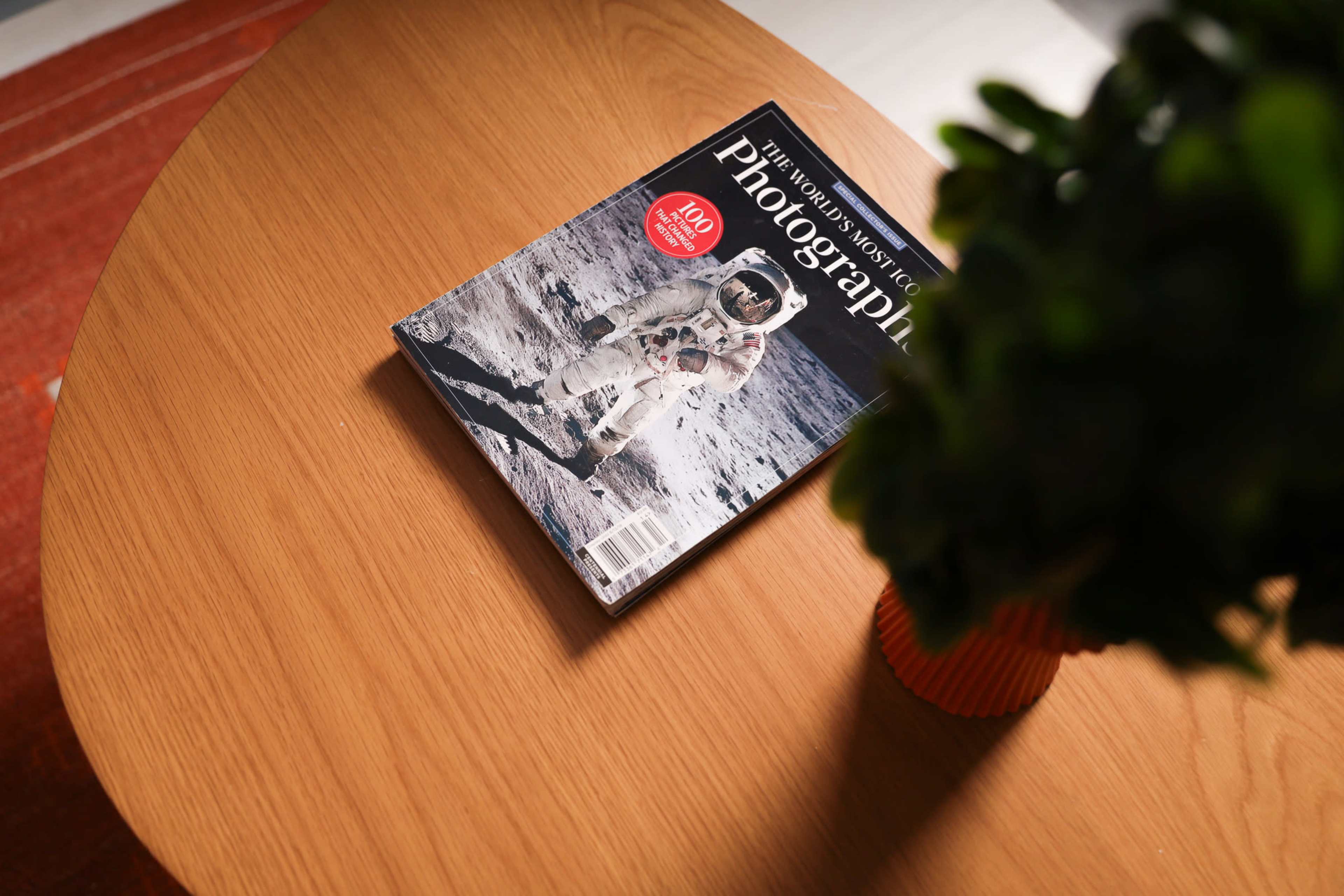 A magazine titled "The World's Most Interesting Photographs" featuring an astronaut on the cover sits on a wooden table next to a plant.