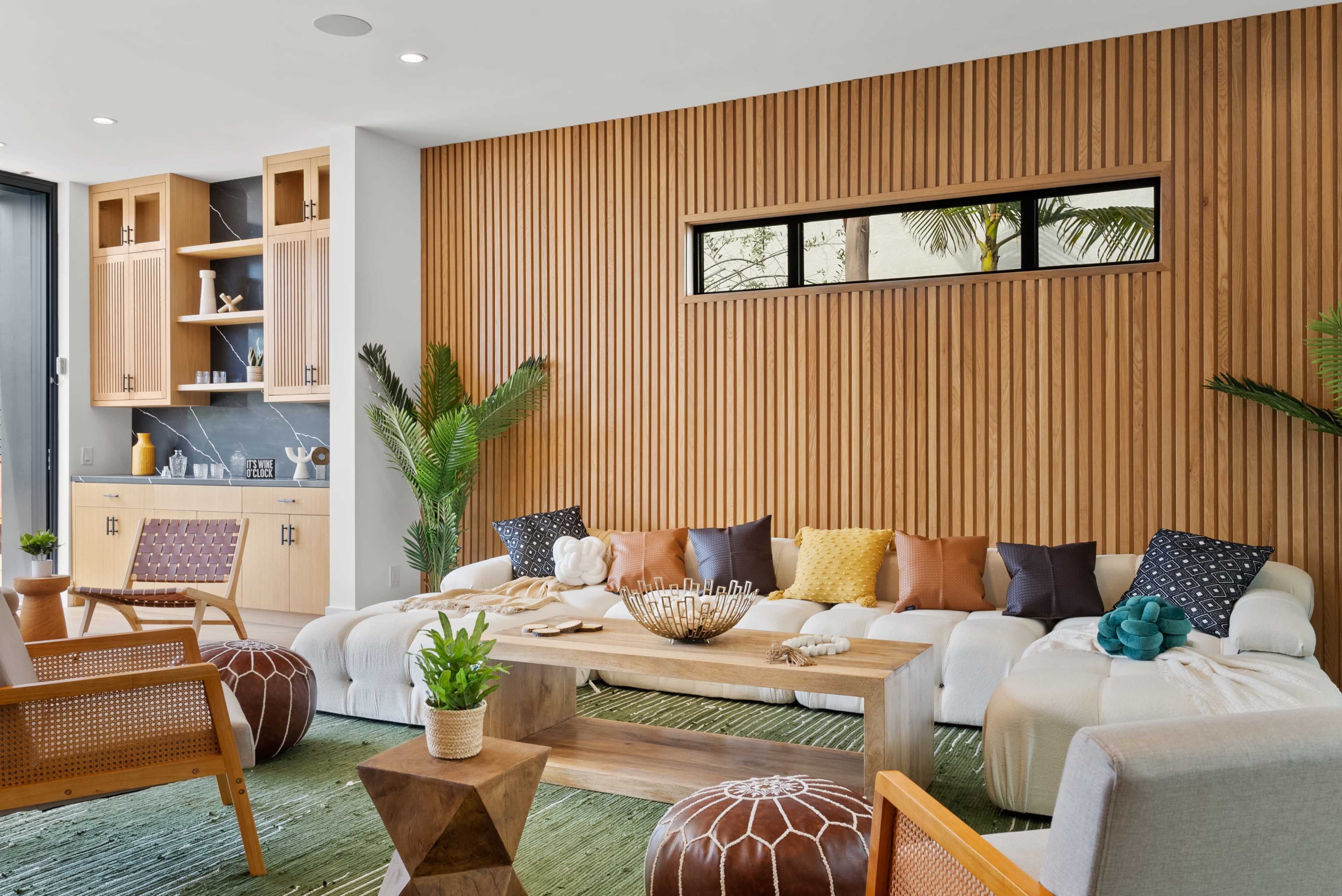 The living room features a wooden accent wall, a sectional sofa with colorful throw pillows, and a wooden coffee table surrounded by chairs and decorative items.