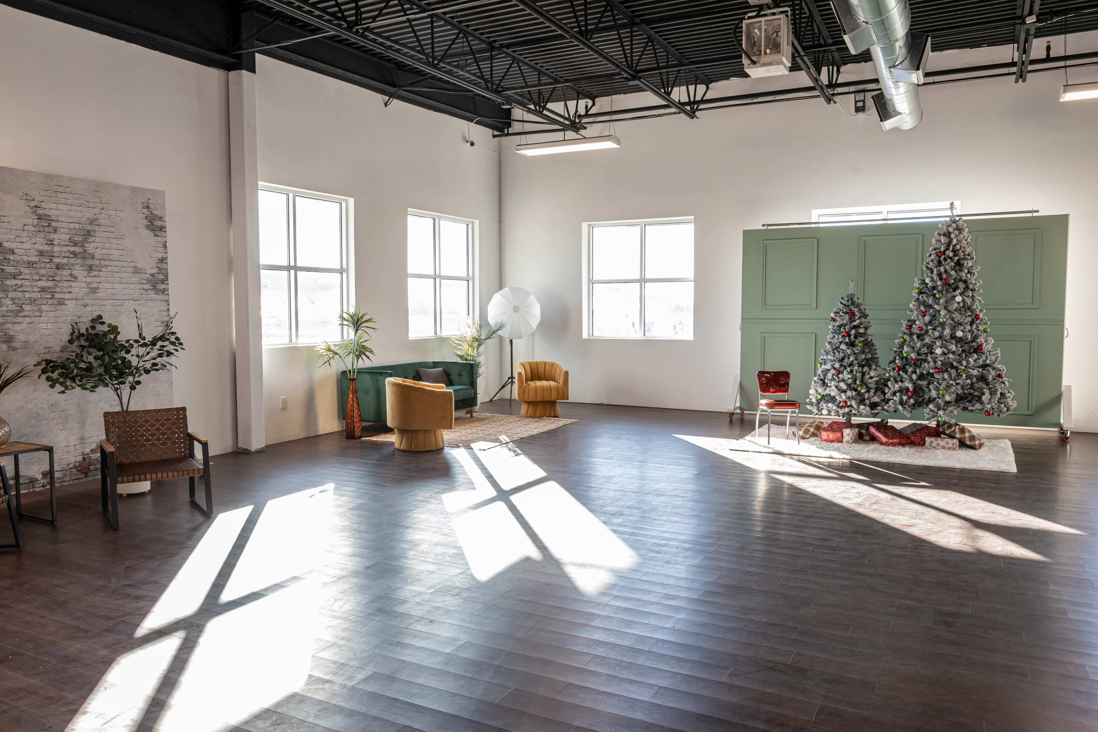The image shows a spacious room with large windows, wooden flooring, a decorated Christmas tree, and various seating arrangements.