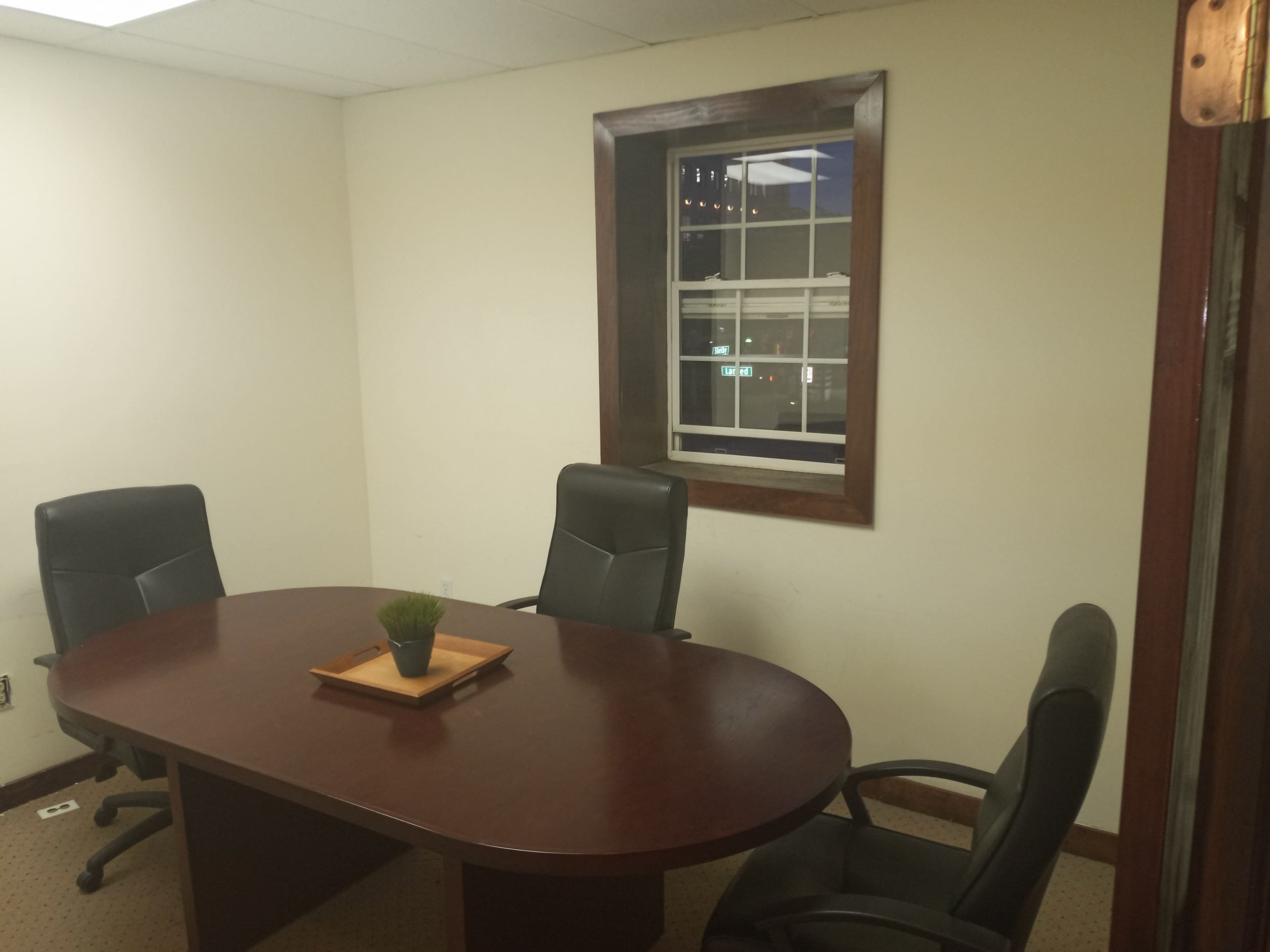 The image shows a small meeting room with a round table and three chairs, featuring a window that overlooks an outdoor scene at night.