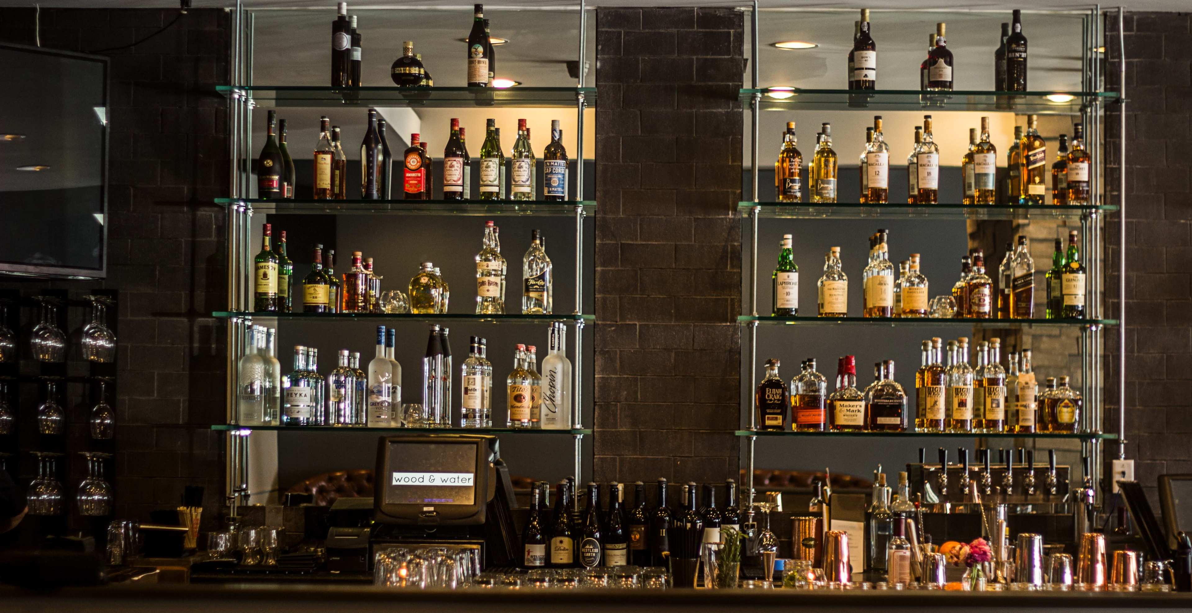 A well-organized bar shelf displaying various bottles of liquor arranged on glass shelves.