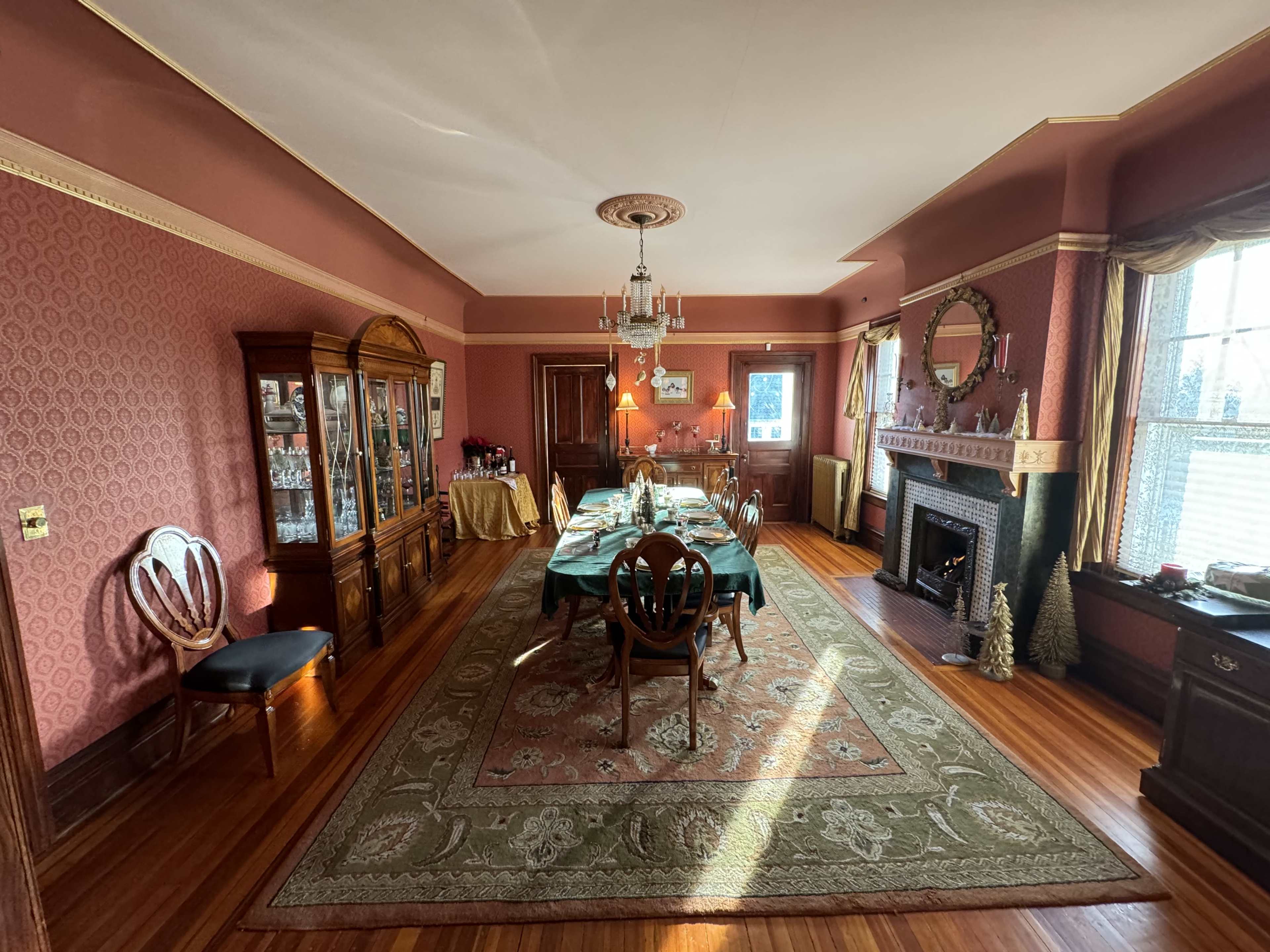 A spacious dining room with a long table set for a meal, surrounded by wooden chairs, and a large cabinet displaying glassware along one wall.