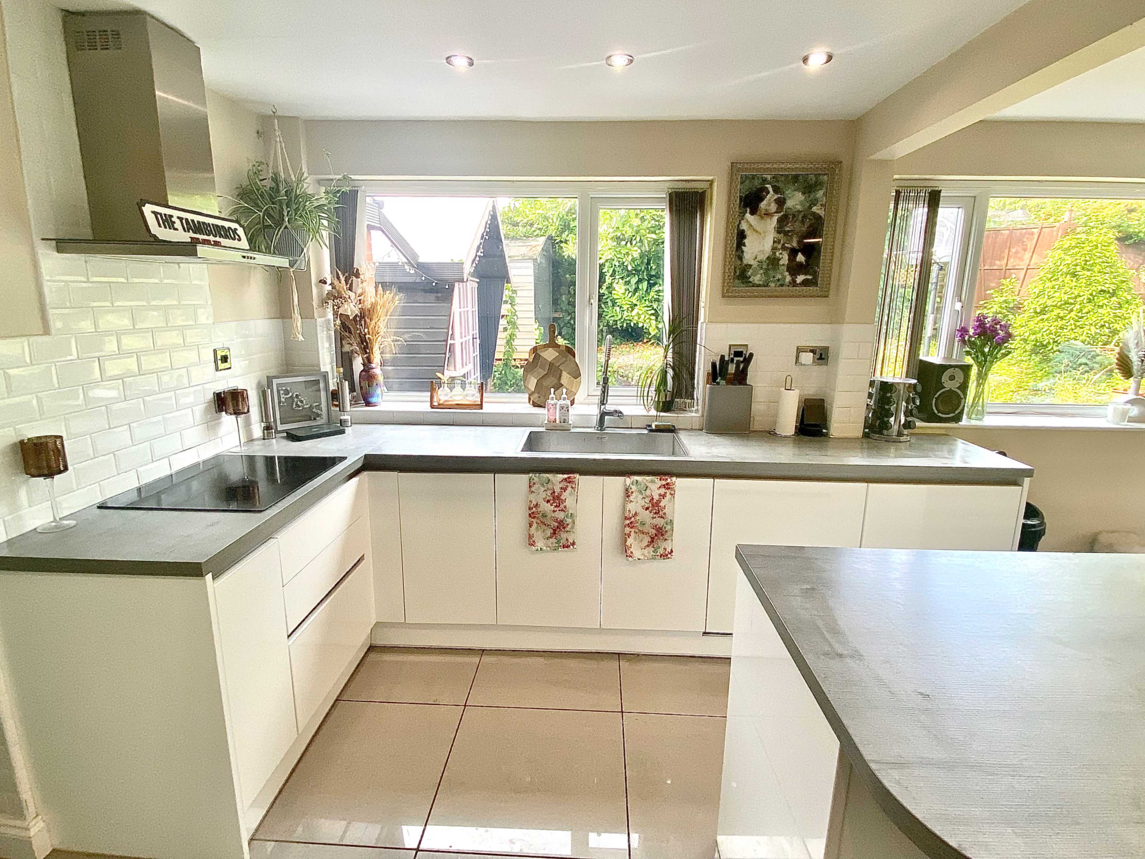 A modern kitchen features white cabinetry, a gray countertop, and large windows that provide natural light, with greenery visible outside.