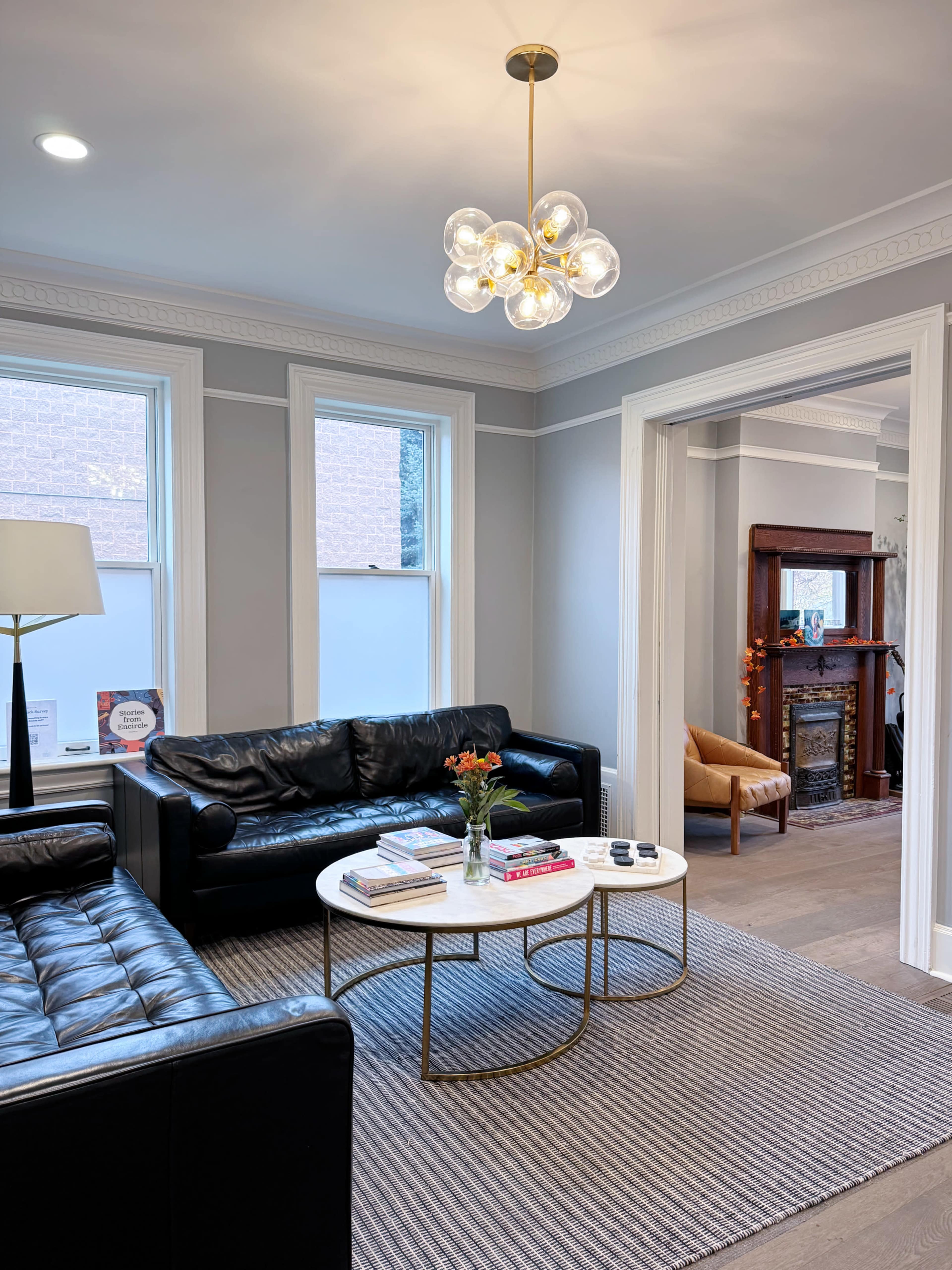 A modern living room with black leather sofas, a round coffee table with magazines, and a decorative light fixture hanging from the ceiling.
