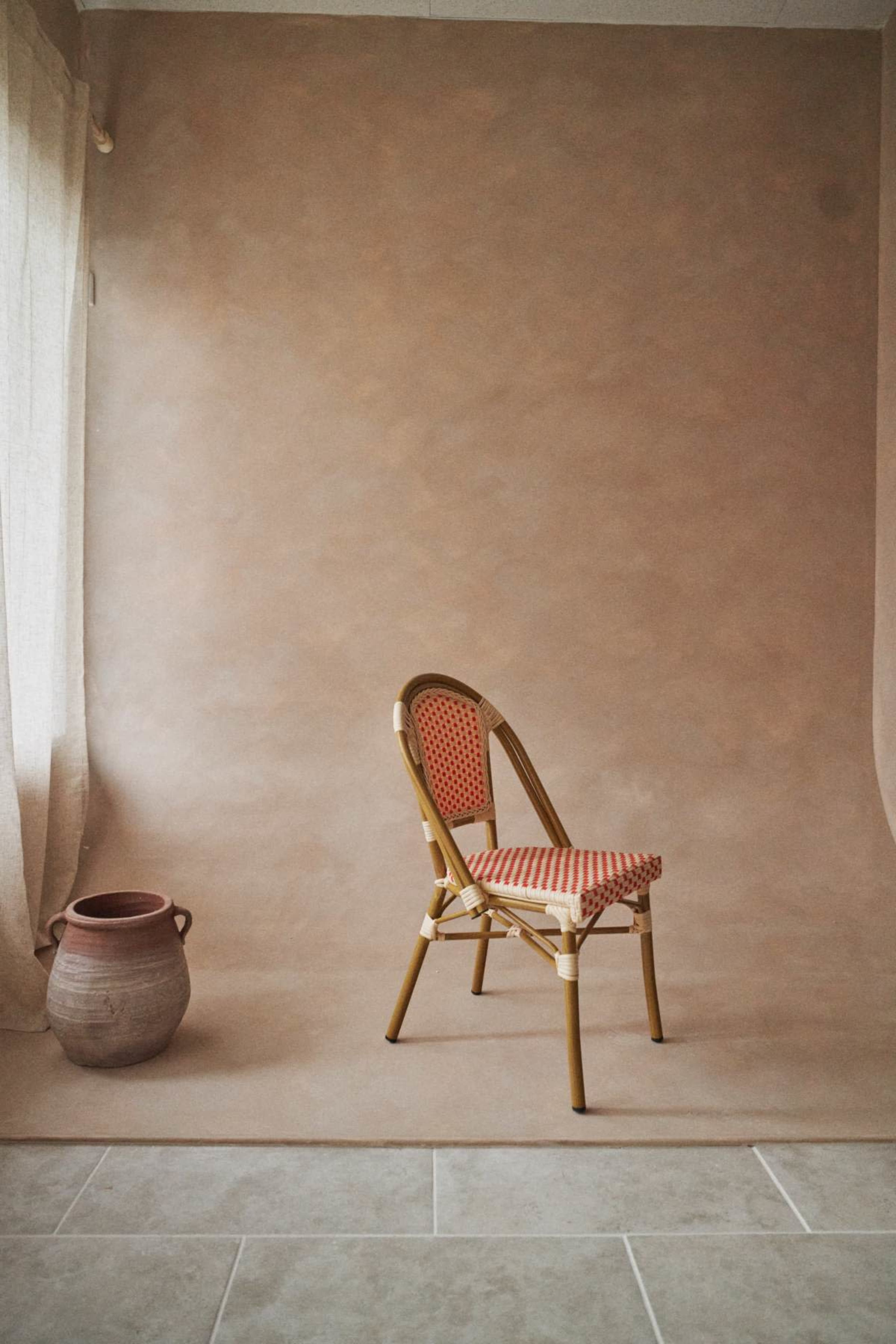 A single patterned chair is positioned near a clay pot against a backdrop of smooth, neutral-toned walls and flooring.