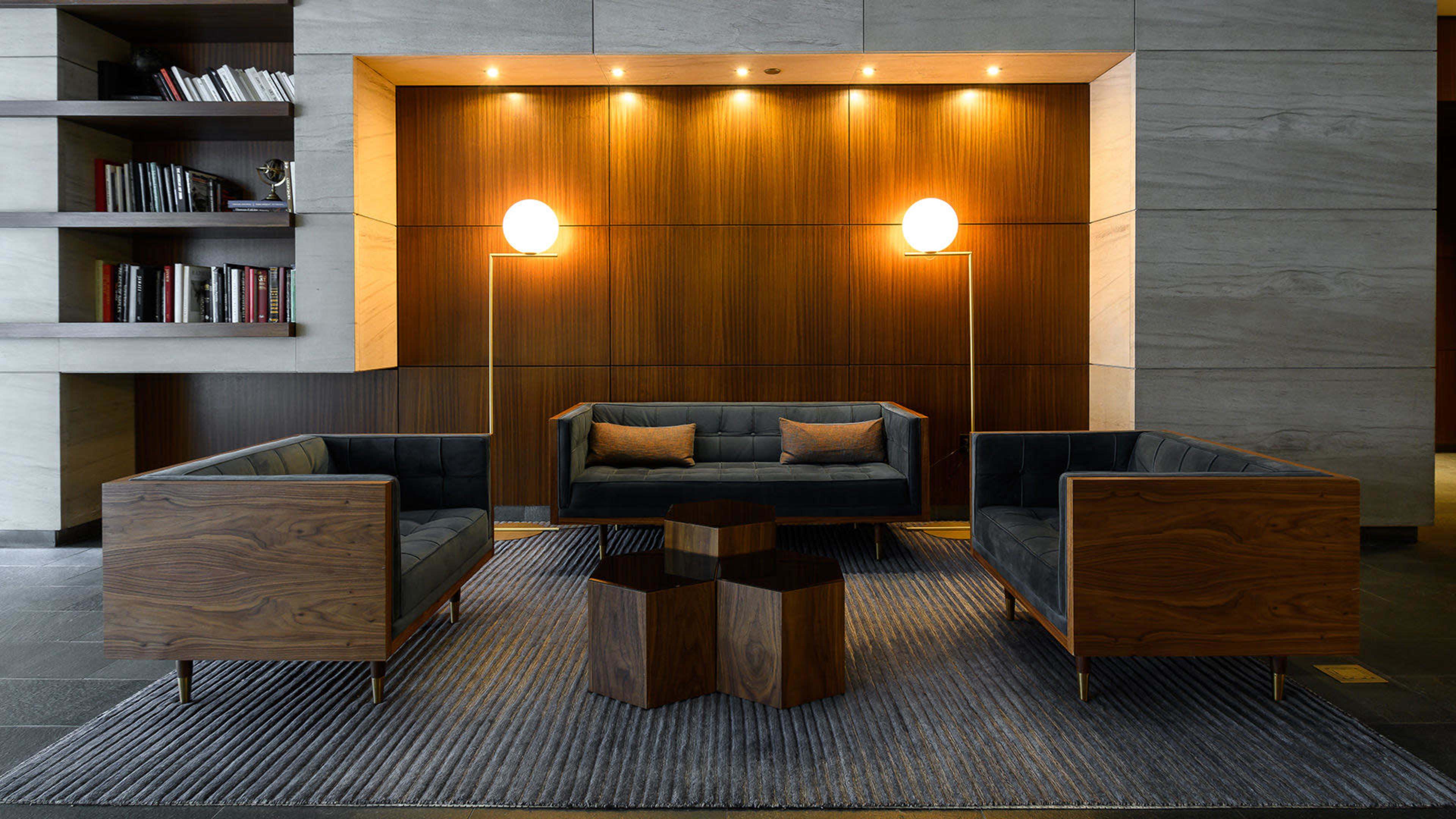 The image features a modern lounge area with two upholstered sofas, a wooden hexagonal coffee table, and two standing lamps against a wooden-paneled wall.